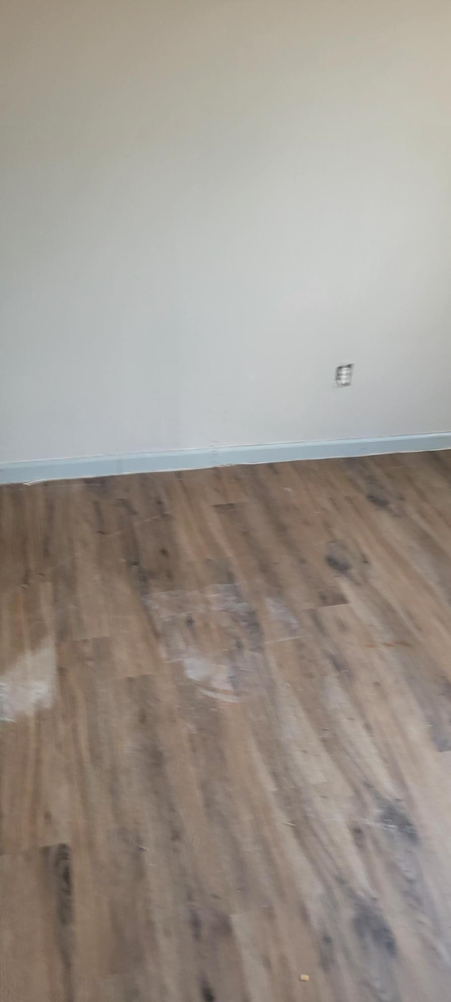 Room with wood-look flooring and light-colored walls. An electrical outlet is visible.