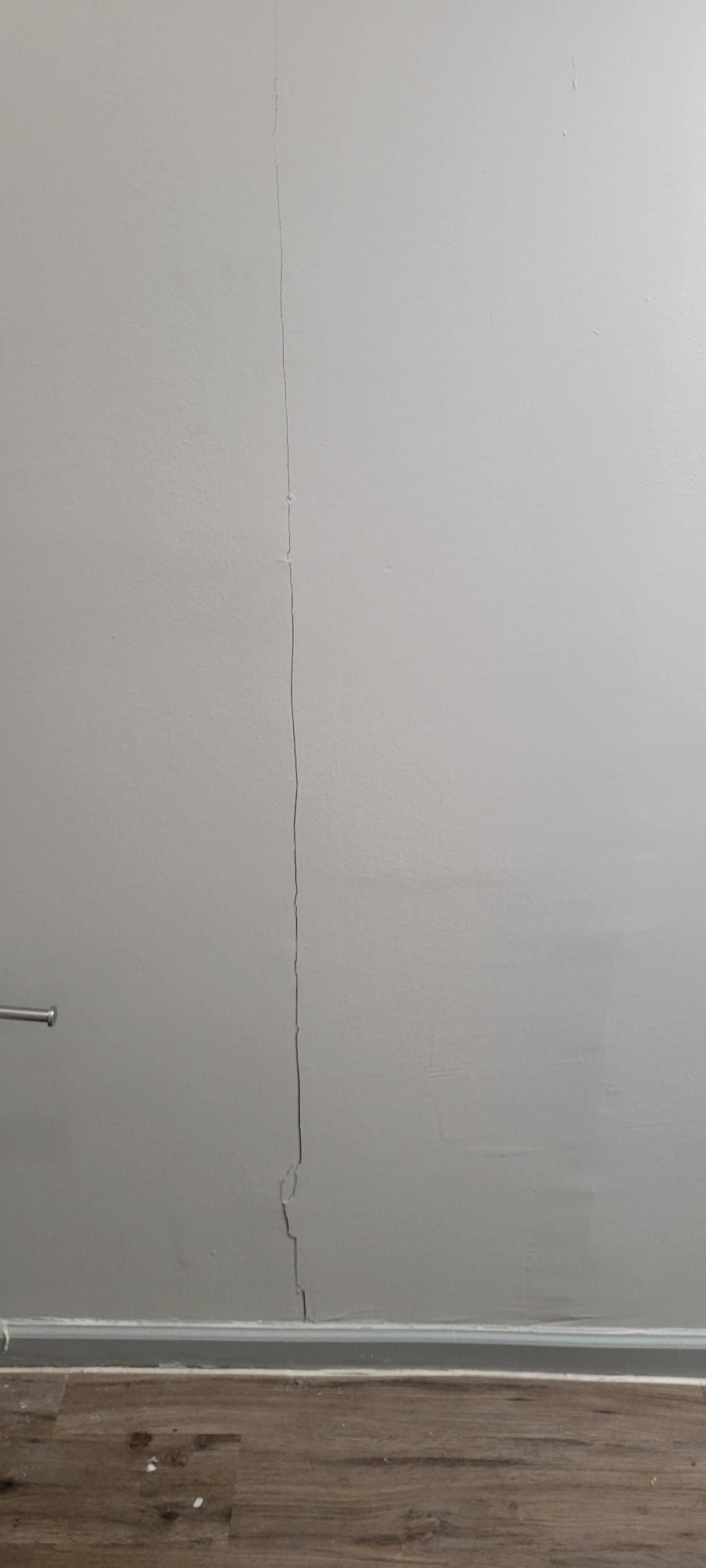 Gray wall with a vertical crack, above brown wooden flooring.