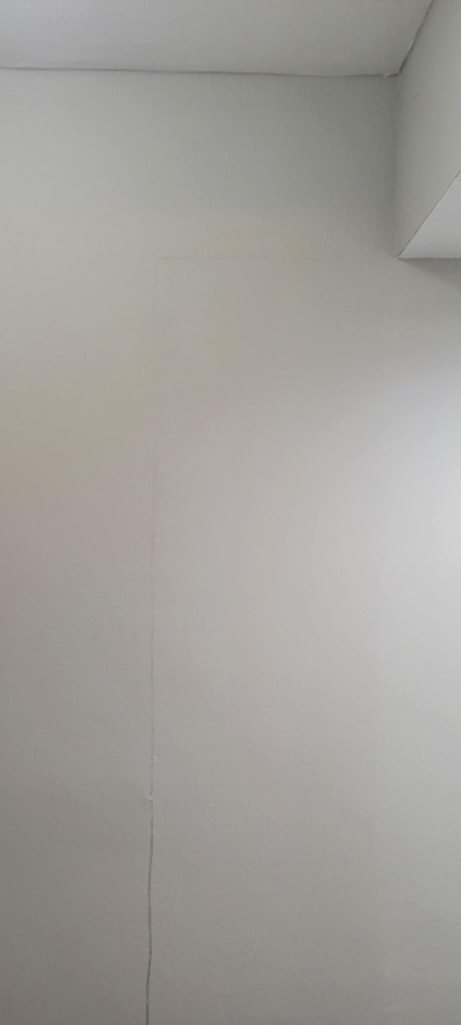 Off-white walls meeting at a corner. A thin, vertical crack is visible on the wall.