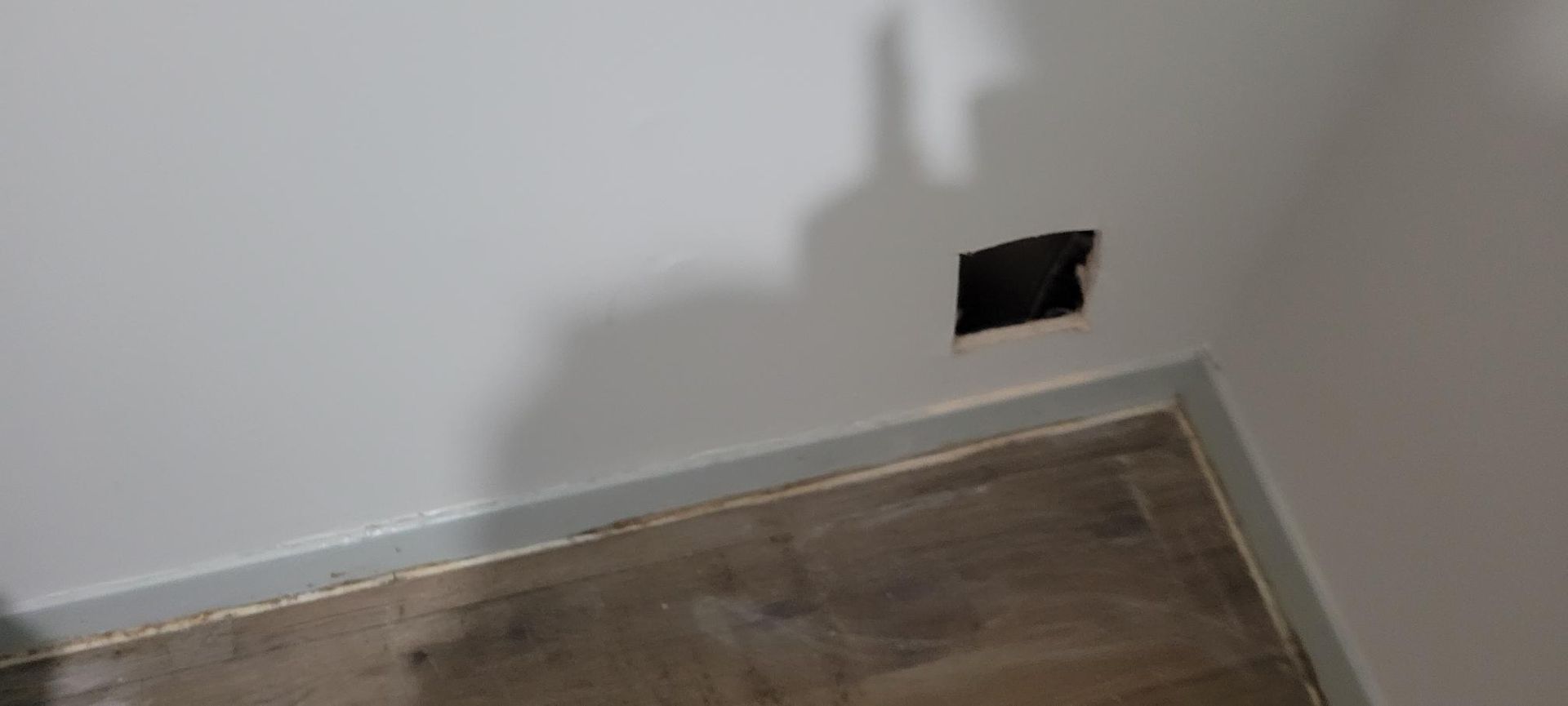 Hole cut into white wall above a wood floor, near a corner.