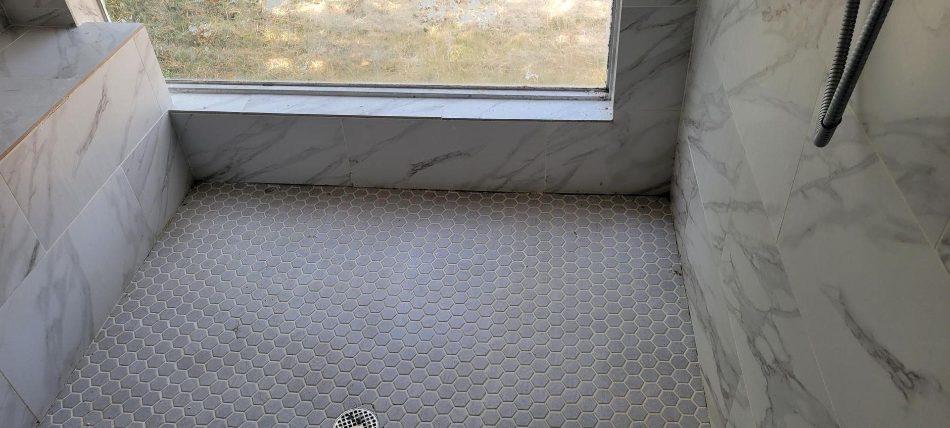 A shower with marble-like walls and a pebble floor, next to a window with condensation.