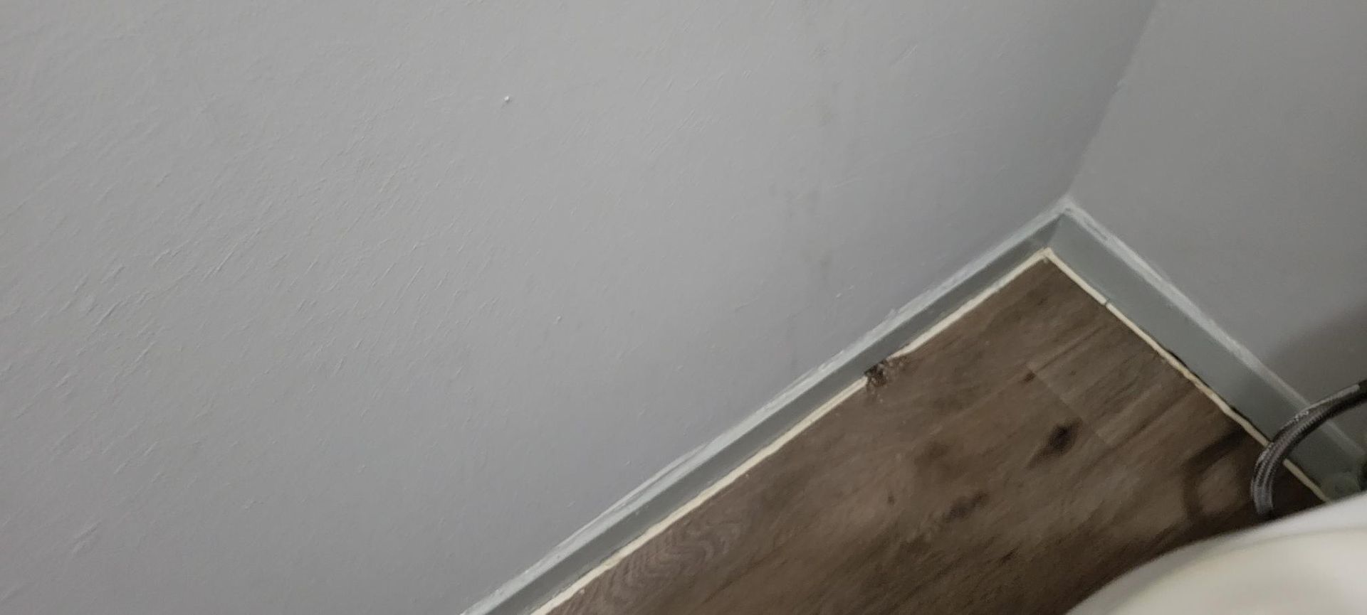 Corner of a room with white ceiling and wooden floor; a white trim outlines the floor.