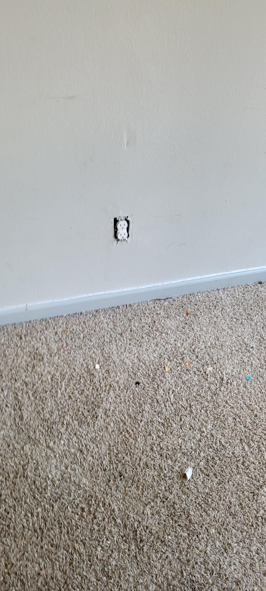 An empty electrical outlet box in a white wall above a carpeted floor.