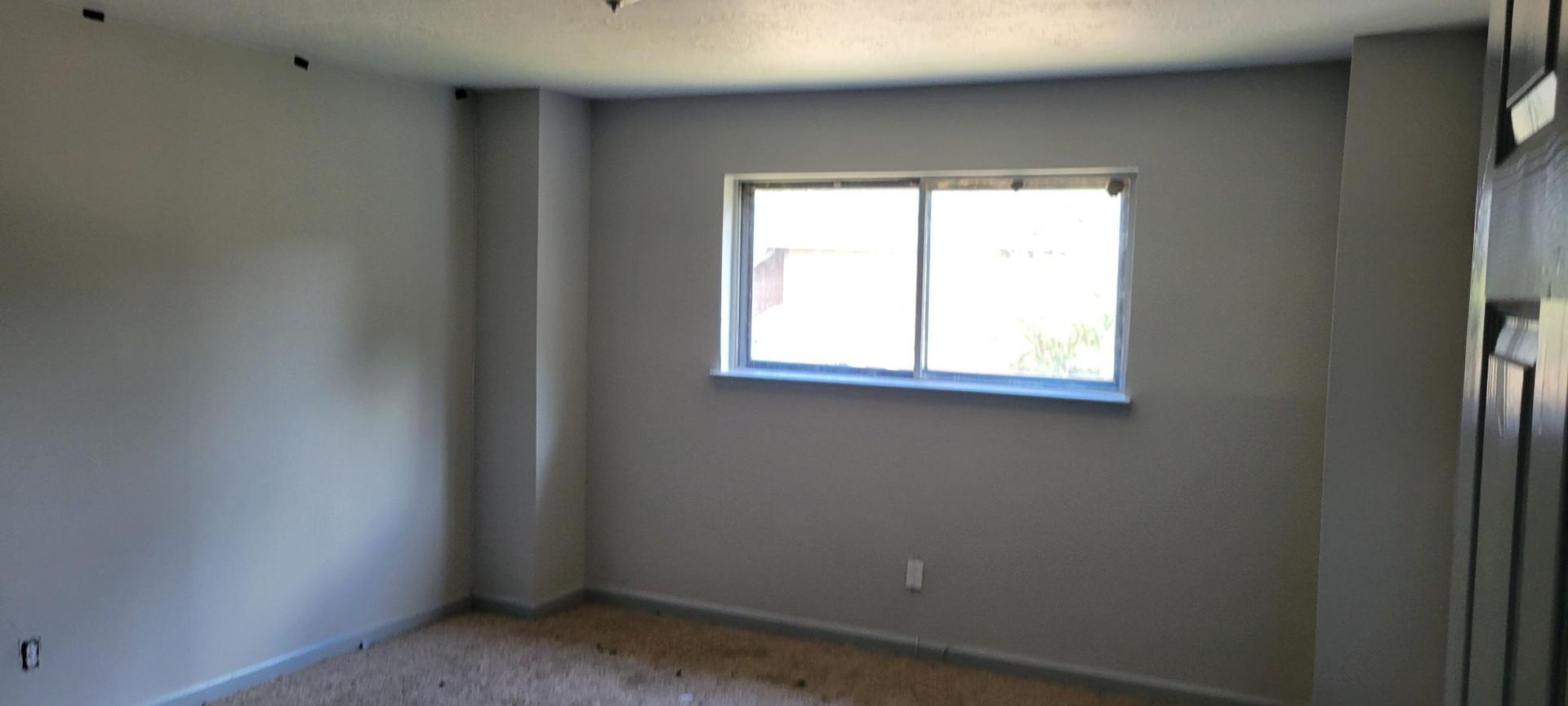 Empty room with a window, painted gray walls, beige carpet.