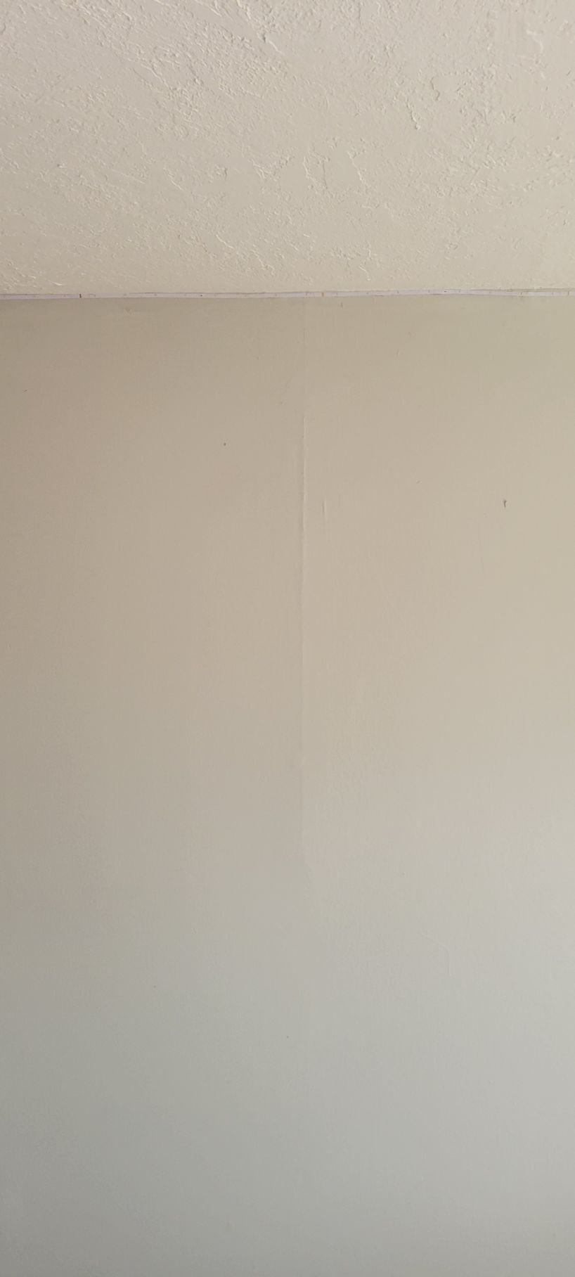 A wall painted beige. Above is a textured white ceiling.