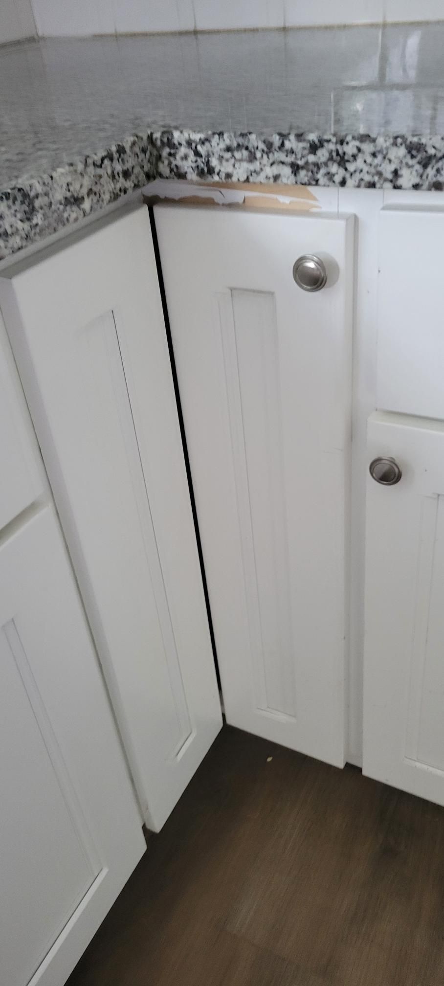 White kitchen cabinets in a corner with a granite countertop and dark wood floor.