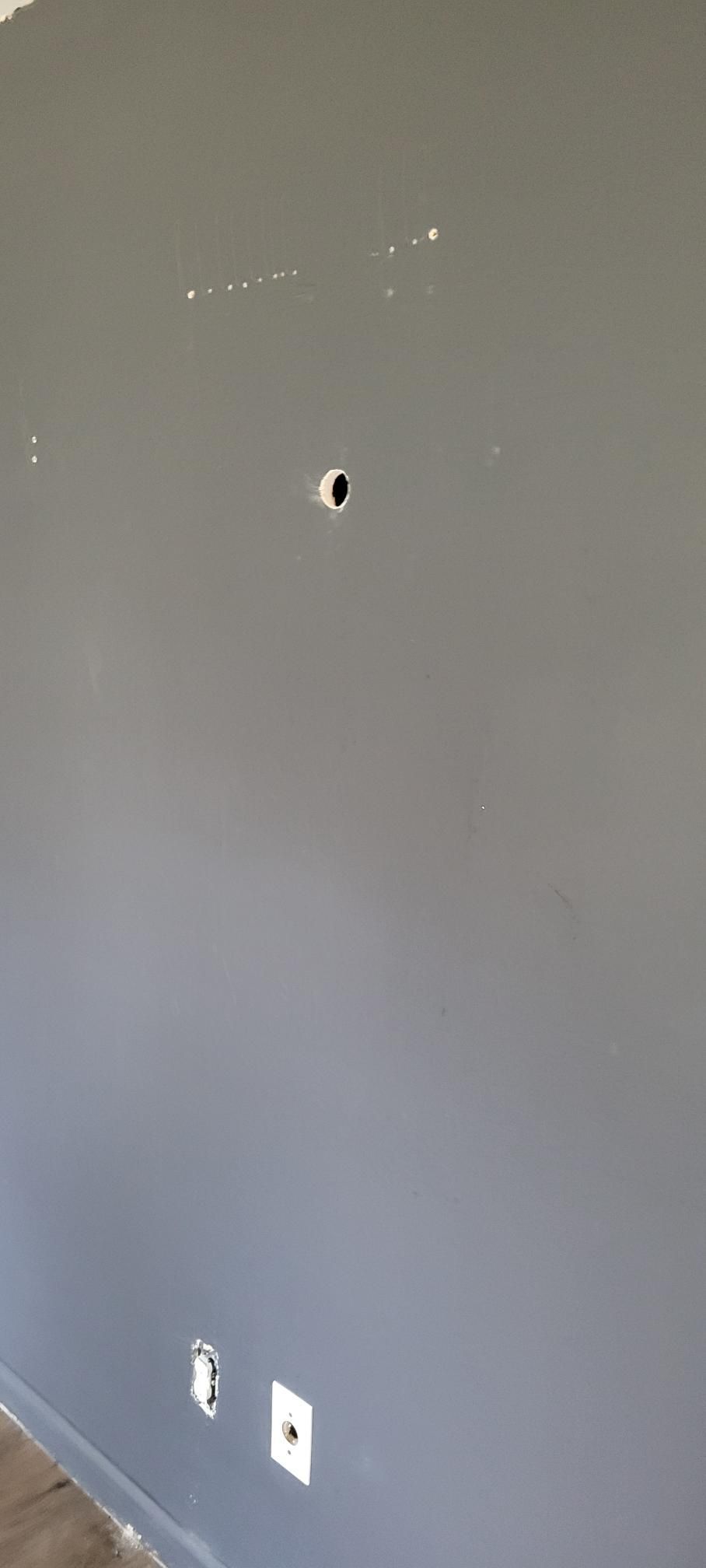 Gray wall with a hole in the center, electrical outlets at the bottom.