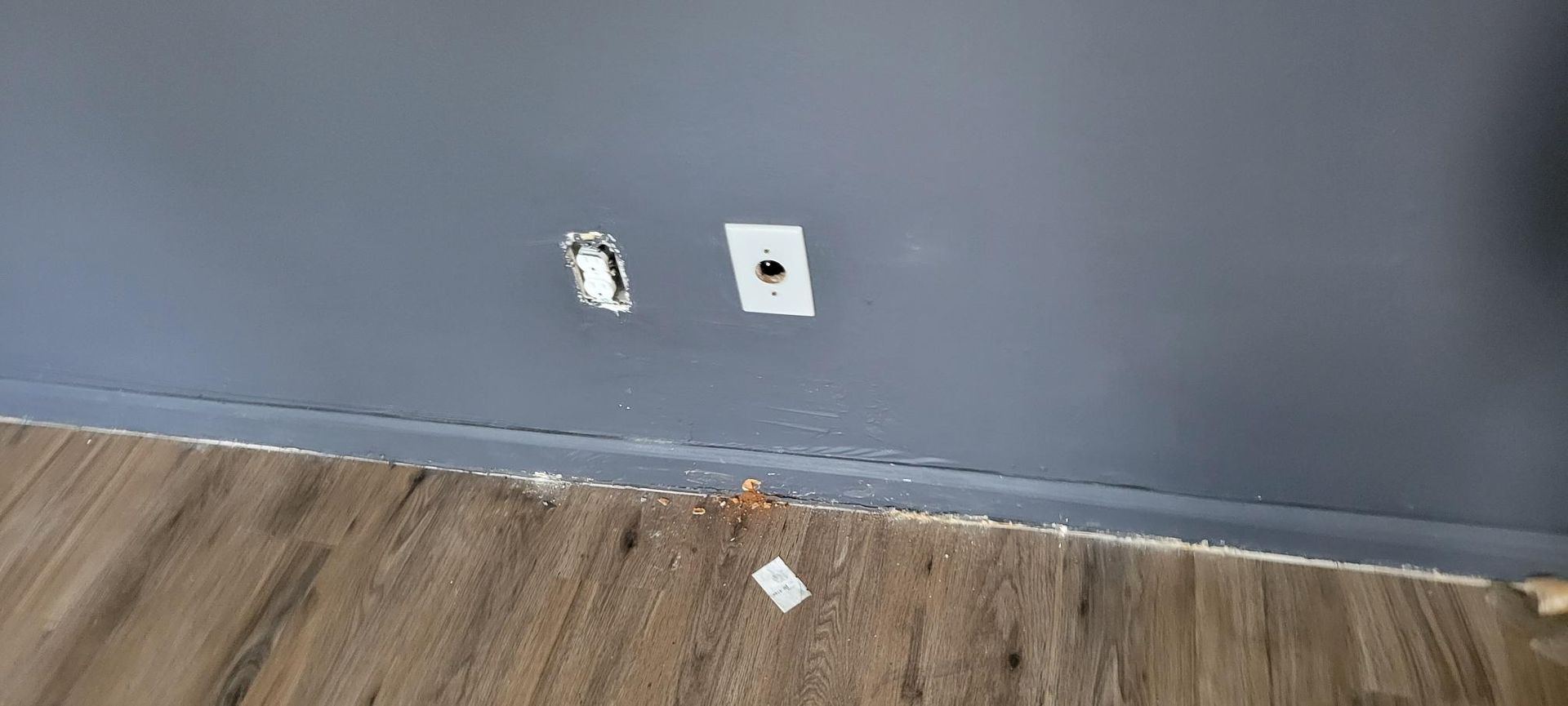 Damaged wall with two holes and a wooden floor.