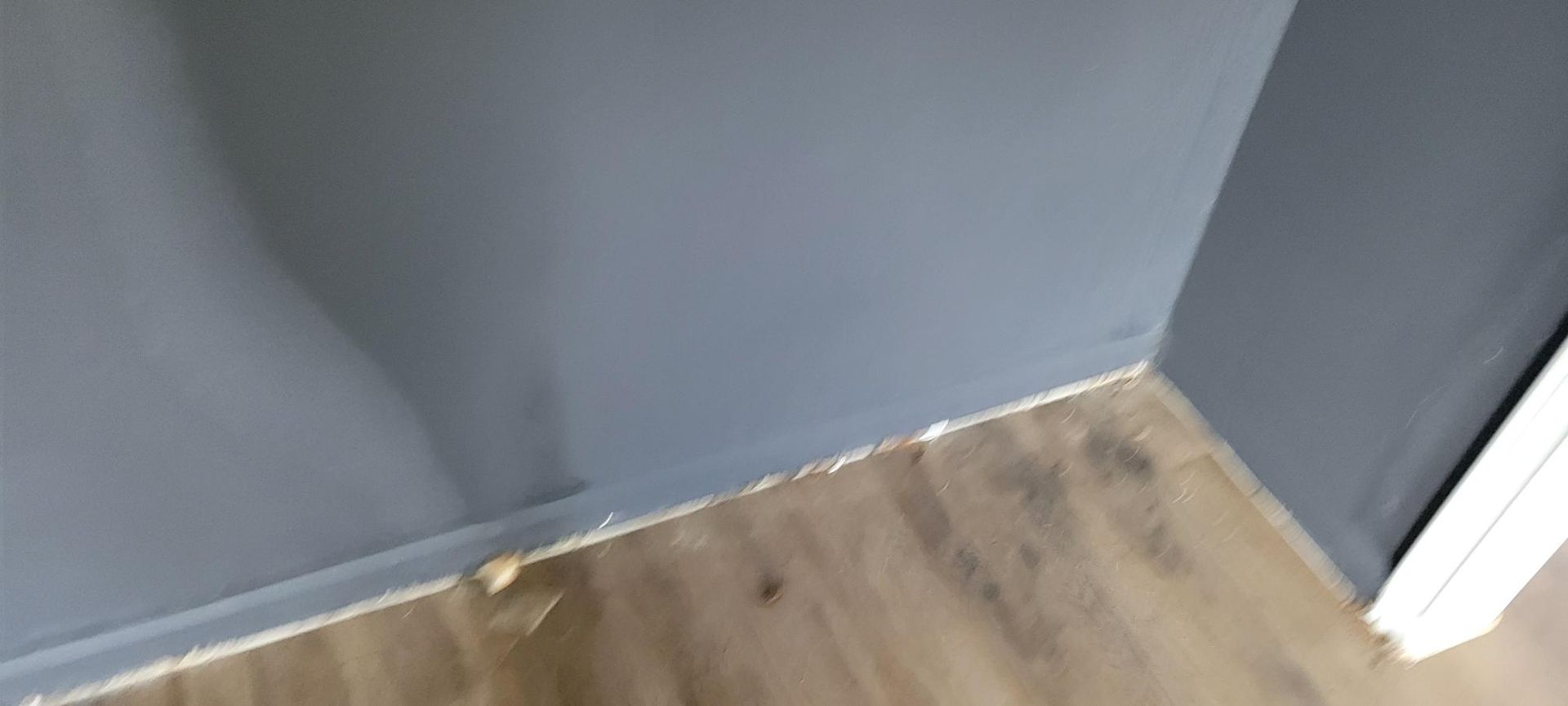 A corner of a room with gray walls and wood-look flooring. White sealant is visible.