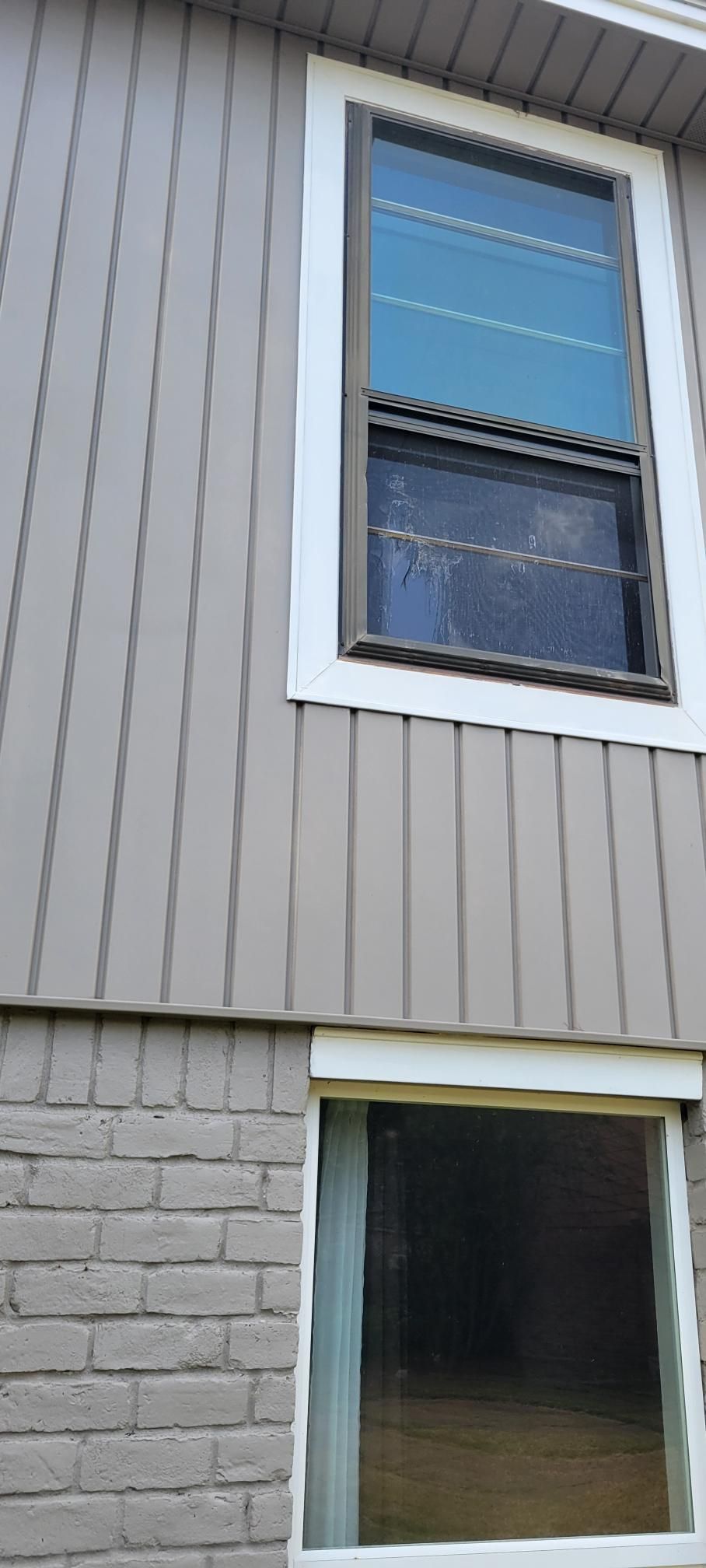 Exterior of a building with two windows: one is framed and tall, the other is smaller and rectangular.