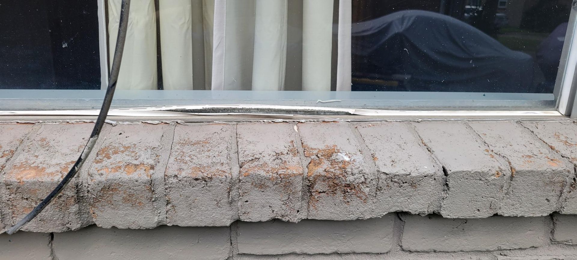 Close-up of a weathered brick windowsill below a window with a sheer curtain.