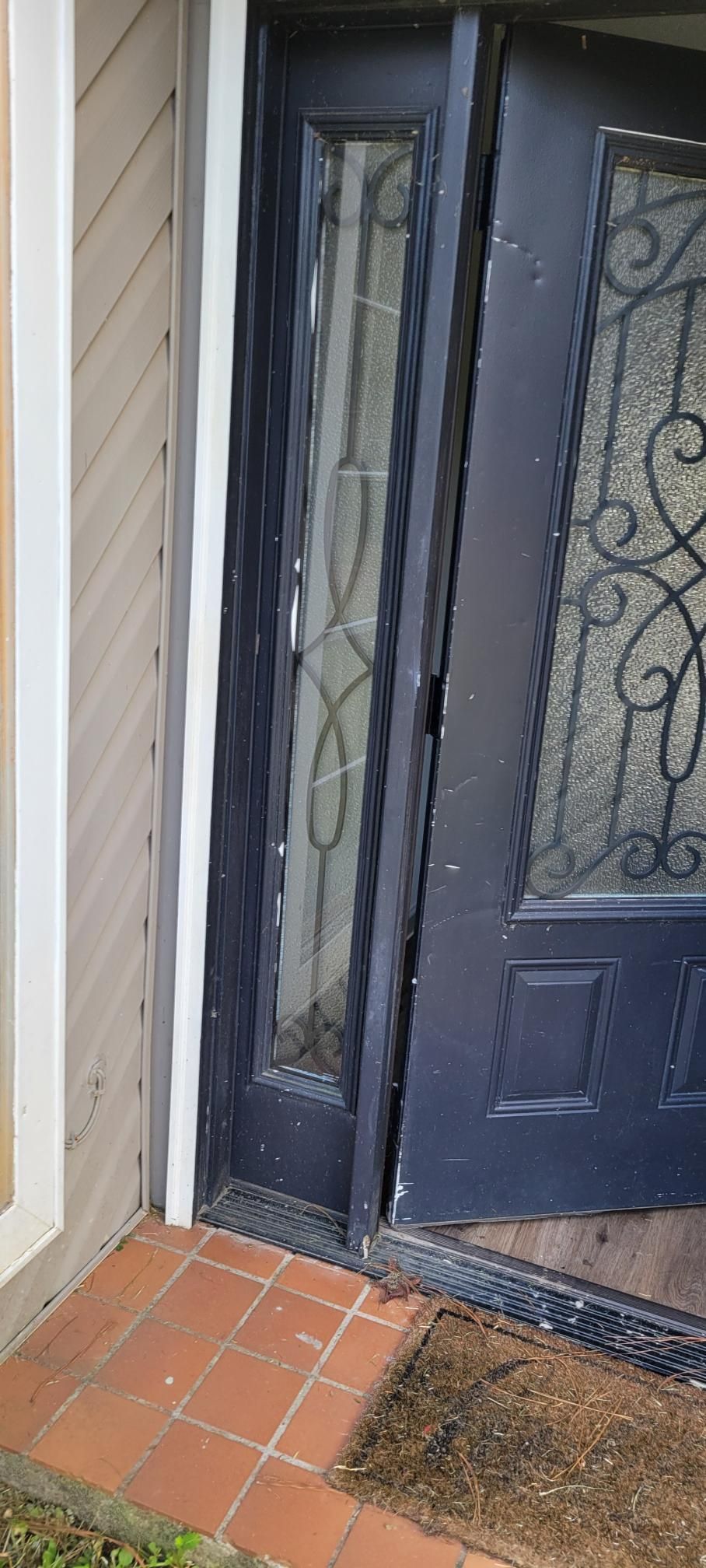 Ajar black front door with sidelight, small brick porch, and beige siding.