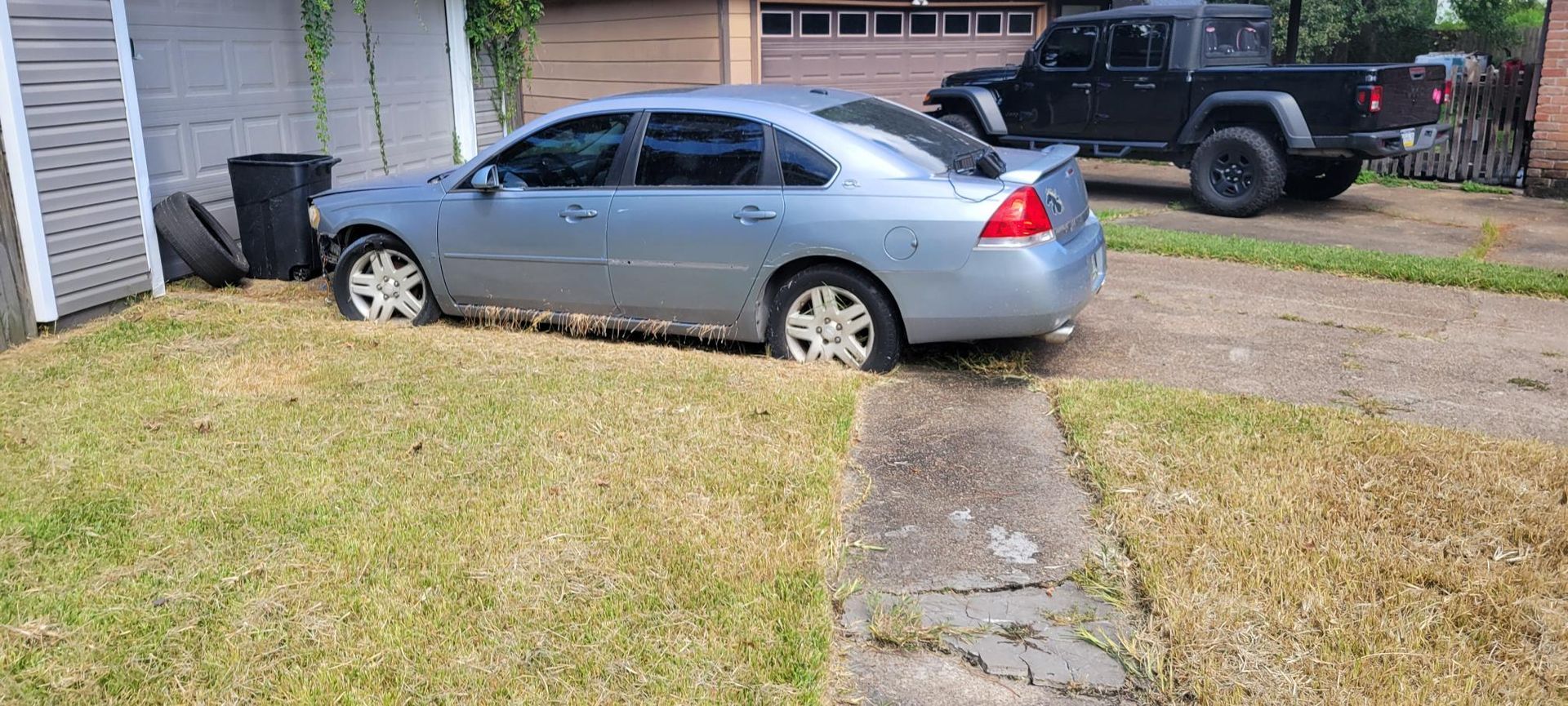 A light blue sedan parked on grass next to a sidewalk and a black pickup truck.