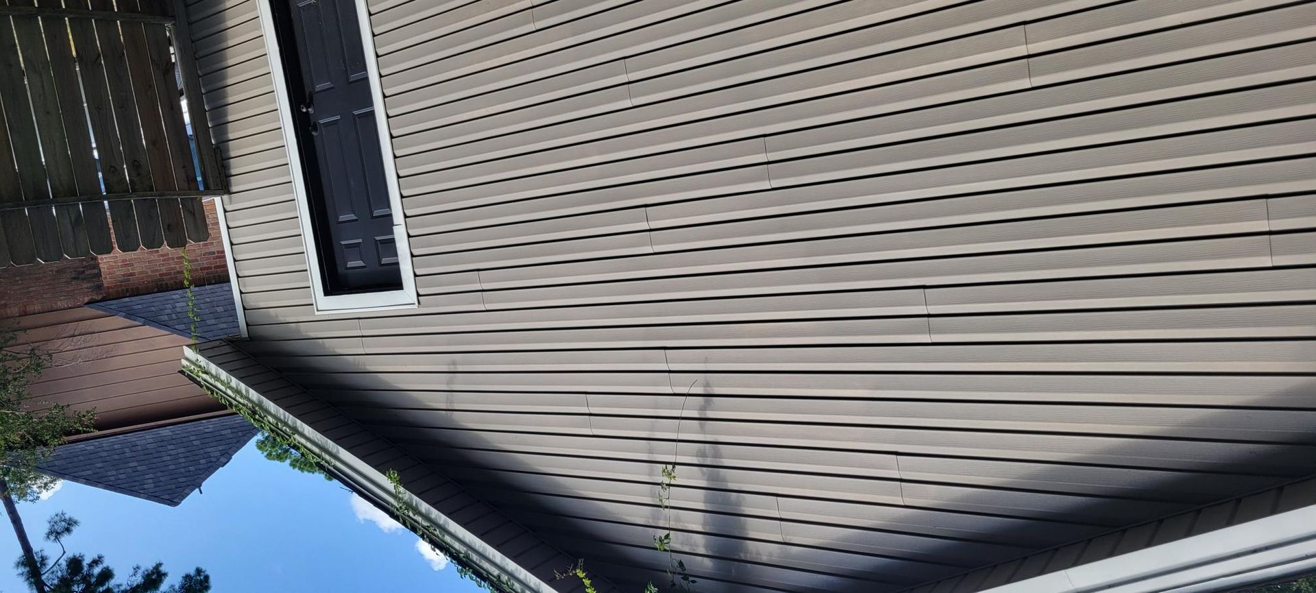 Low-angle view of a building's underside with brown siding, a window, and the sky.