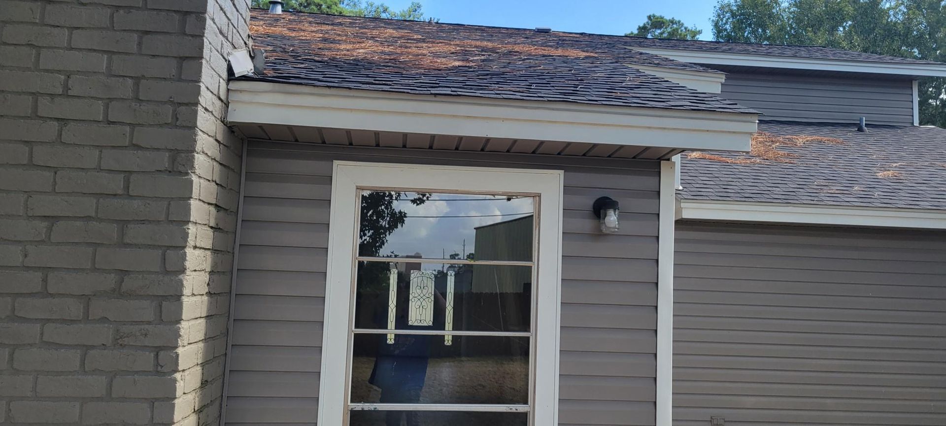 Exterior view of a house, gray siding, a window, and damaged shingles on the roof.