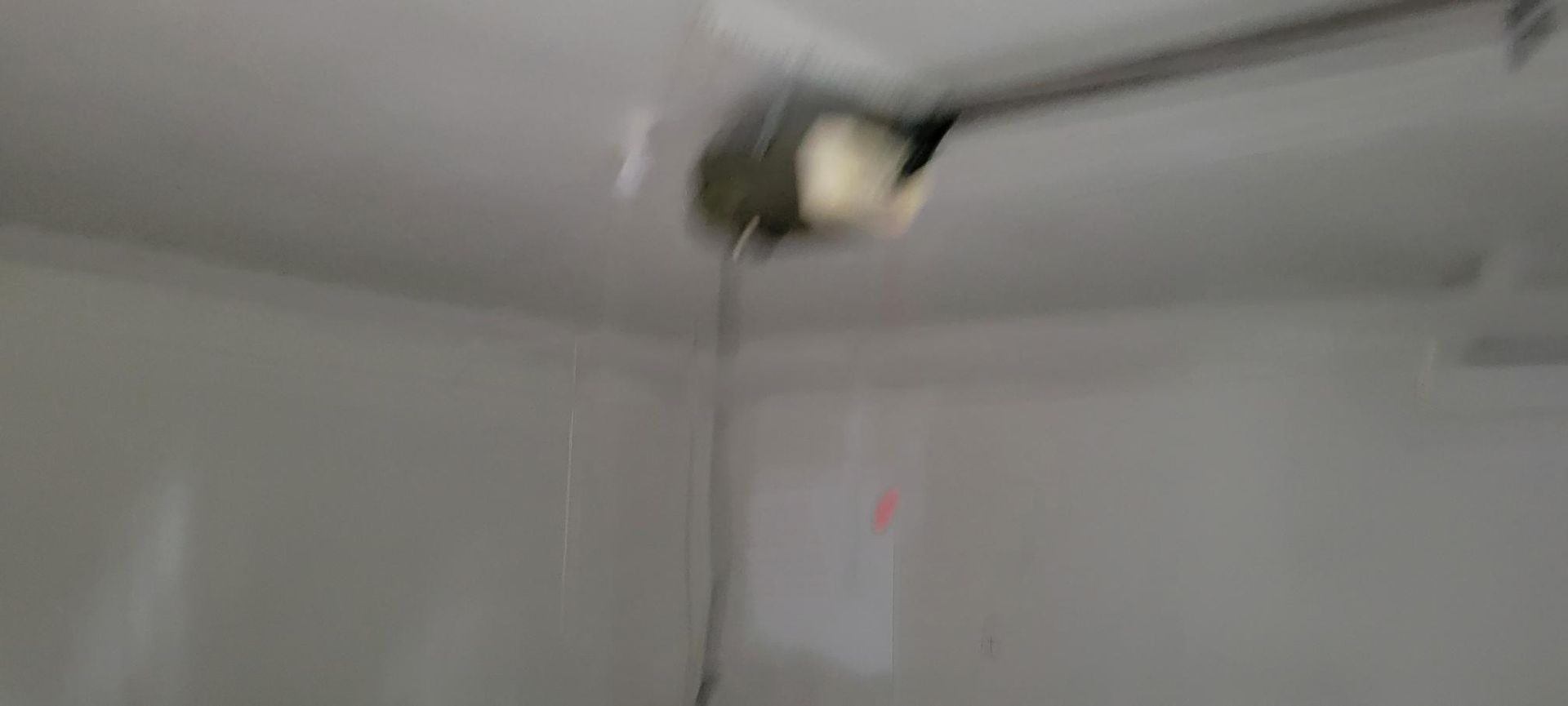 Garage ceiling with garage door opener. The opener has a cable and is attached to a metal bar.
