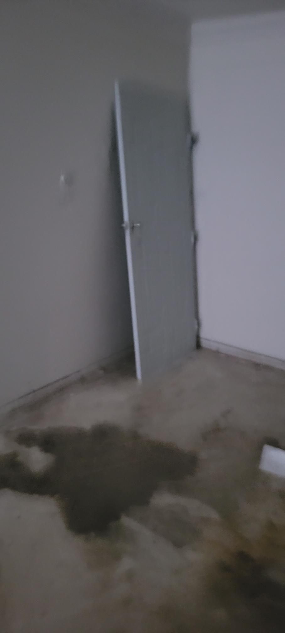 A room with a door propped against a wall and a dark liquid stain on the floor.
