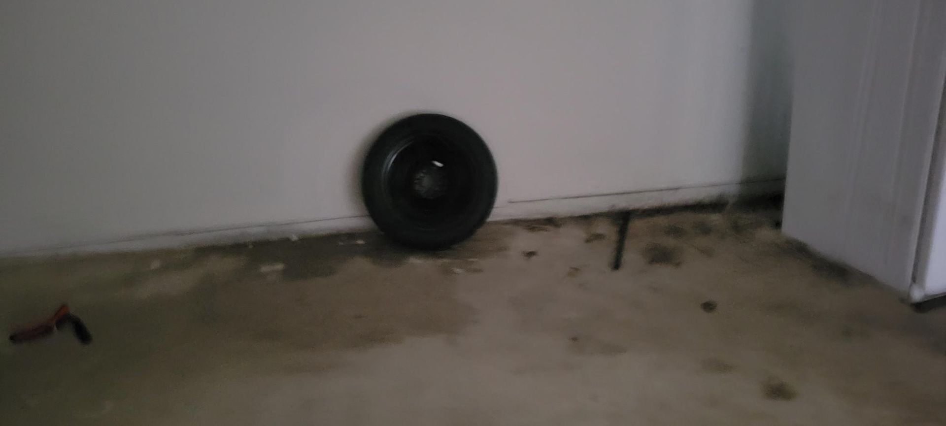 Spare tire leaning against a white wall in a garage.