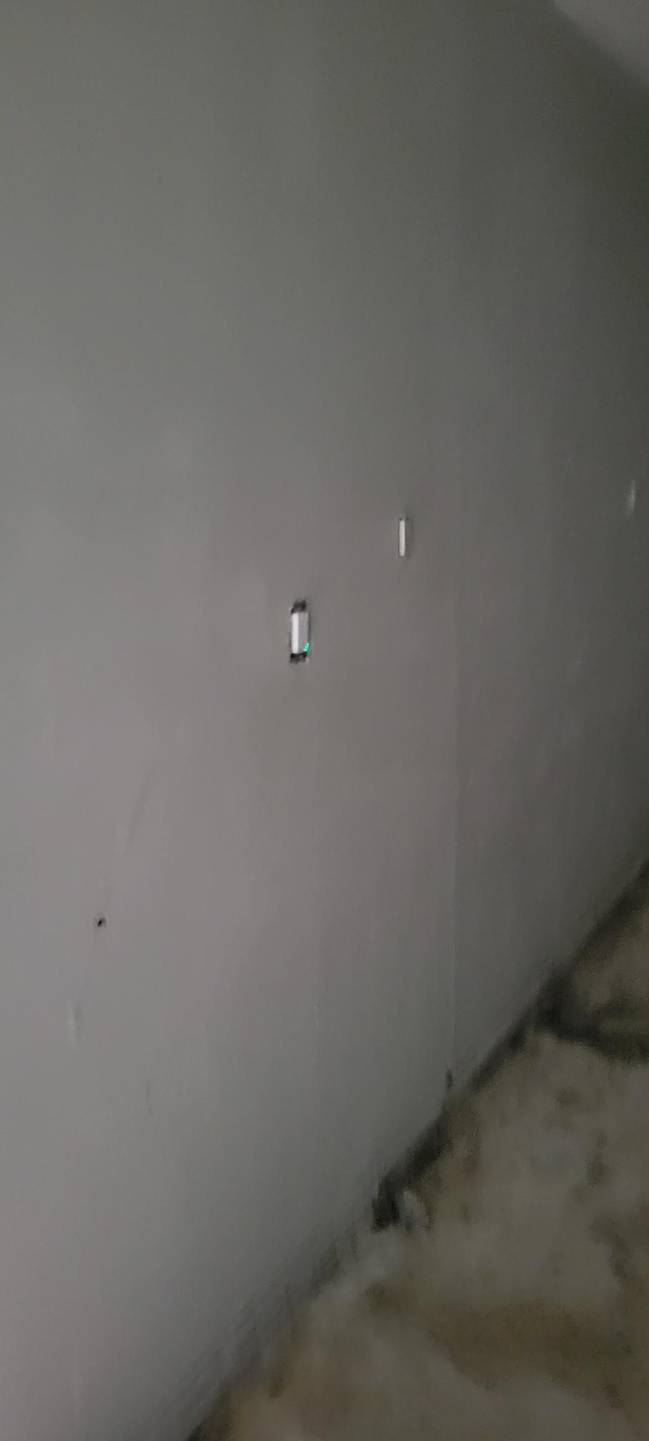 A light-colored wall with several small marks and a small rectangular object. The corner of the room is visible.