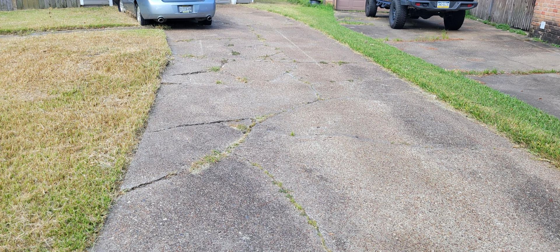 Driveway with two vehicles parked, green grass borders the concrete path.