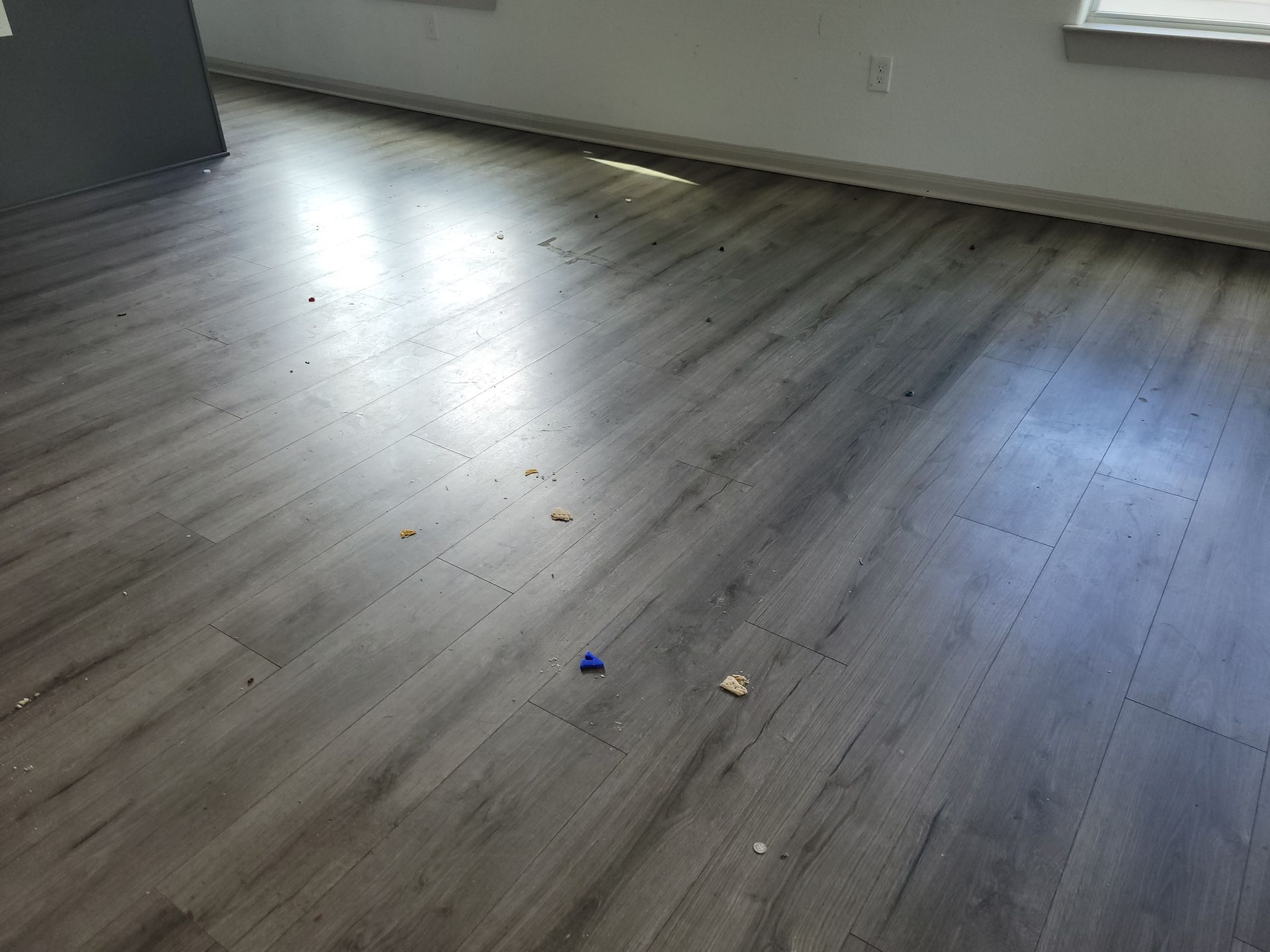 Gray vinyl plank flooring with debris, in a room with white walls and a gray wall on the left.