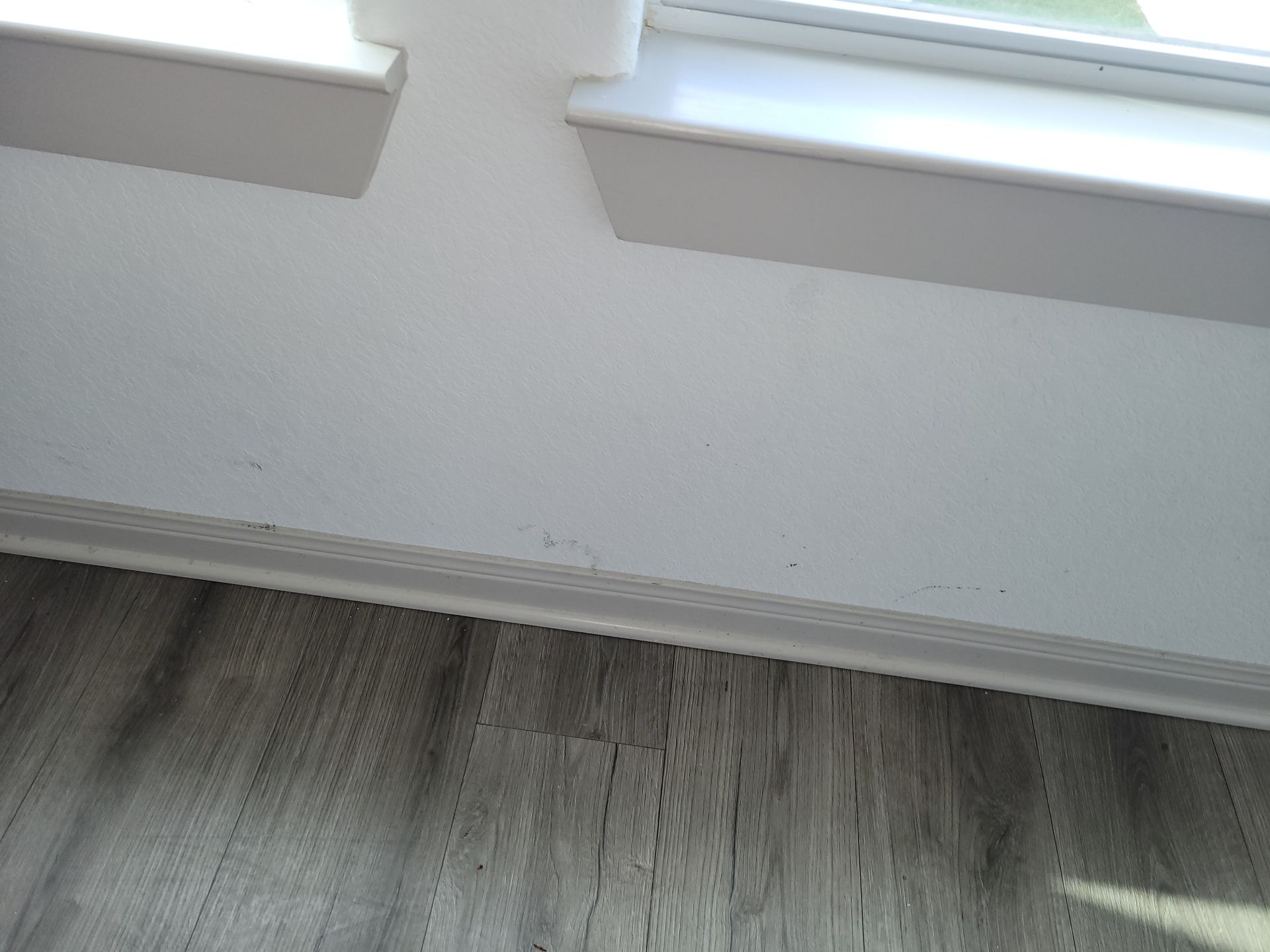 White baseboard and wall with a window sill, next to gray wood-look flooring.