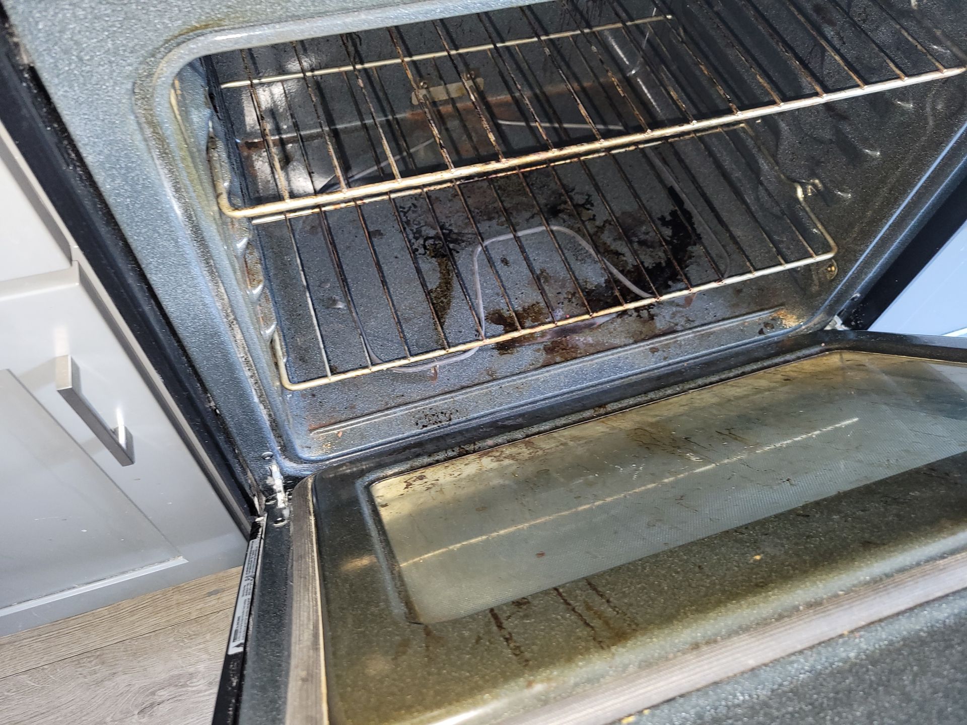 Dirty oven interior with racks and door open. Grime and food residue visible.