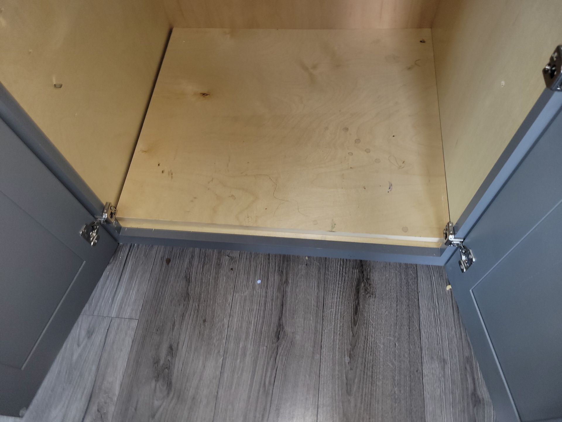 Open cabinet with gray doors, light wood interior, and gray flooring.