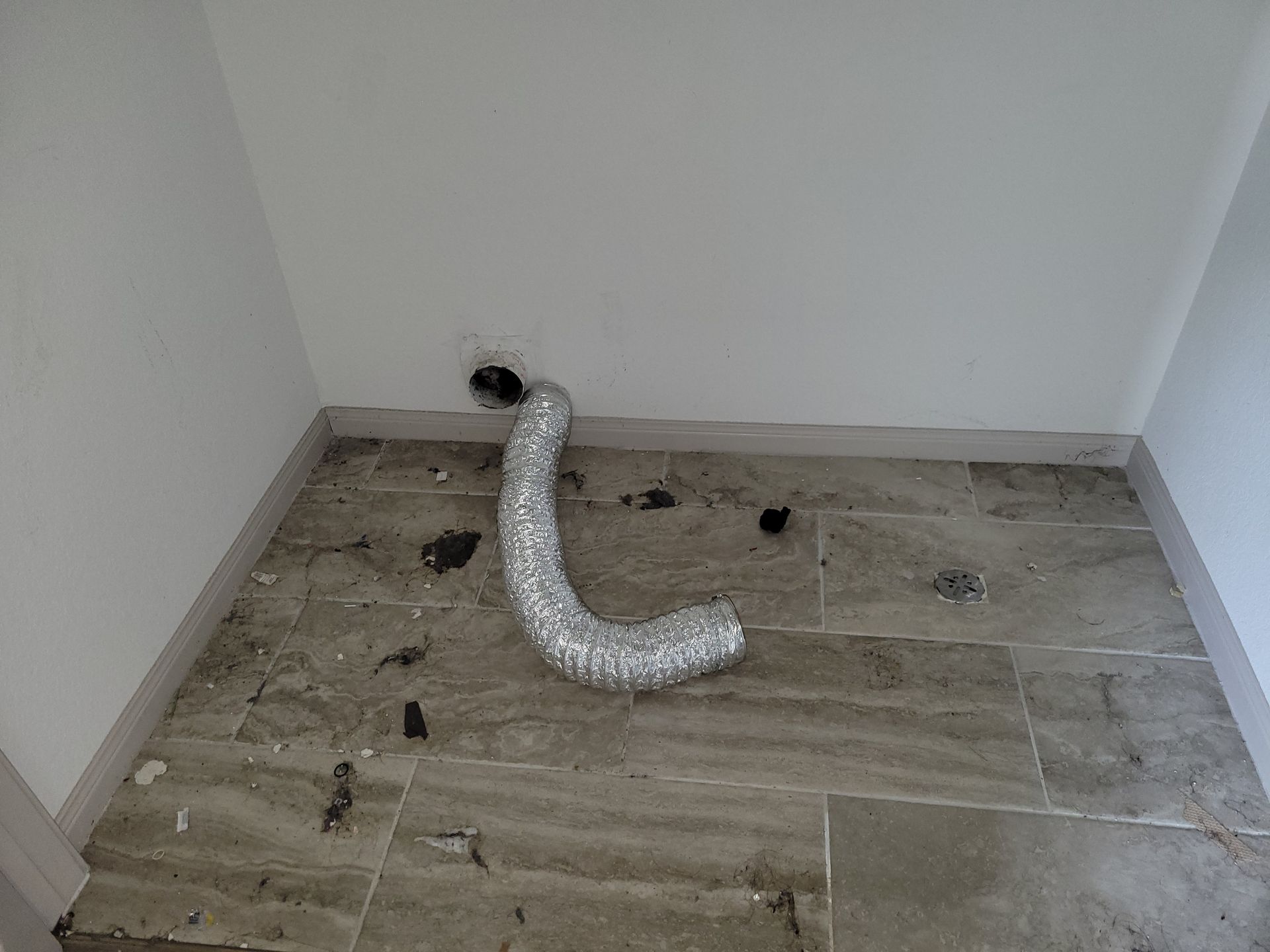 Ventilation duct on tiled floor in a corner with white walls, and a visible hole.