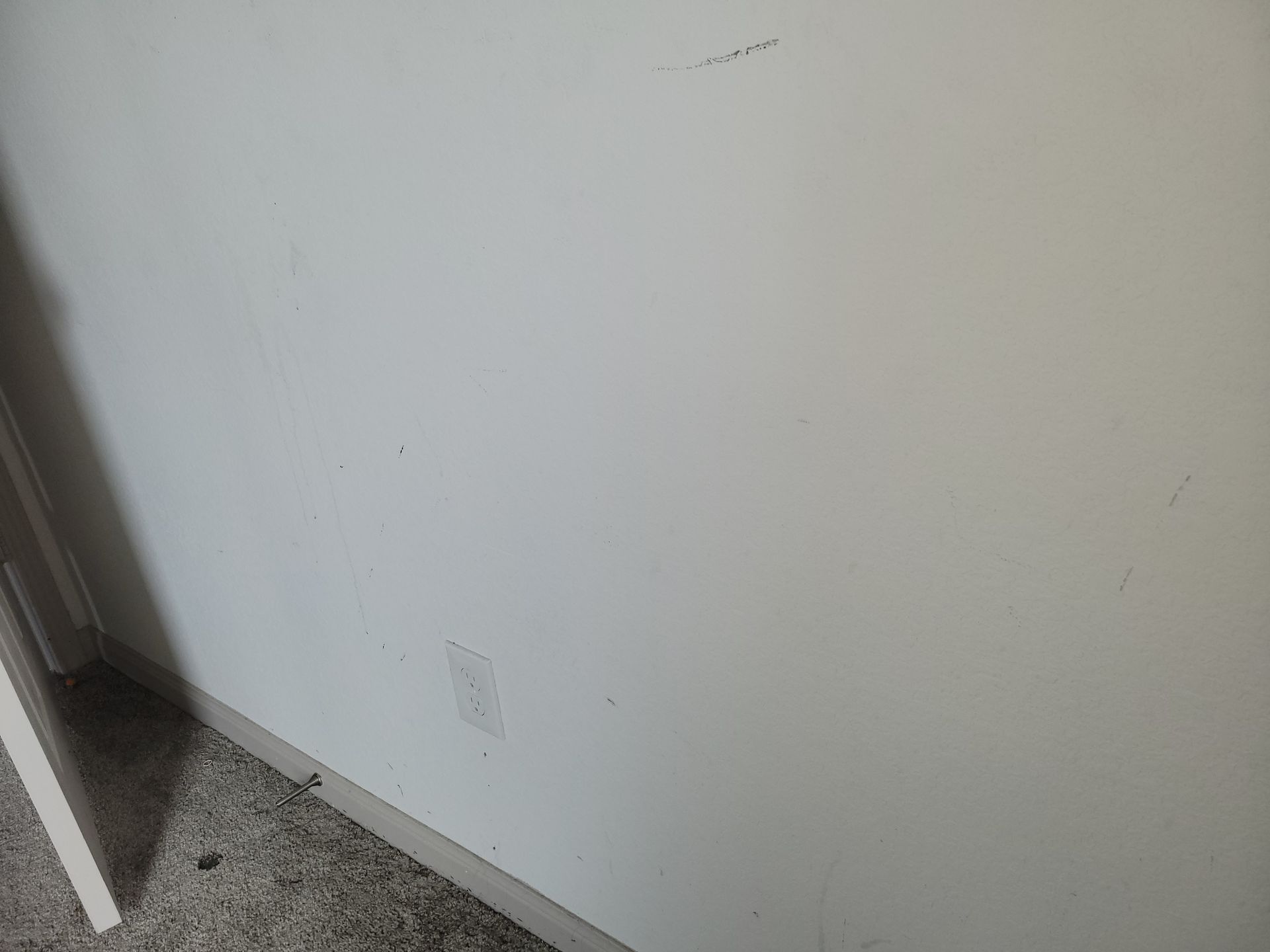 White wall with an electrical outlet and a small door frame; the corner of a room.