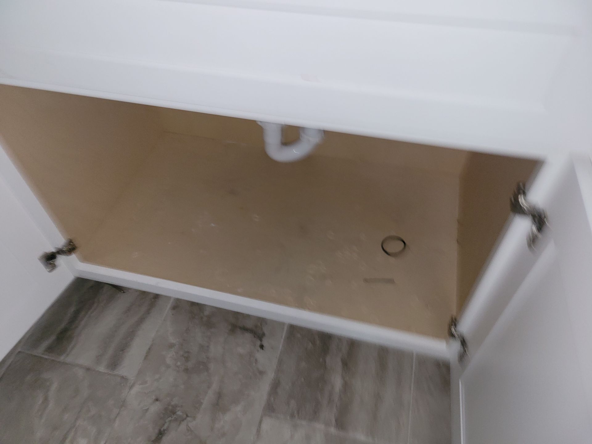 White bathroom cabinet with open doors, revealing plumbing and floor.