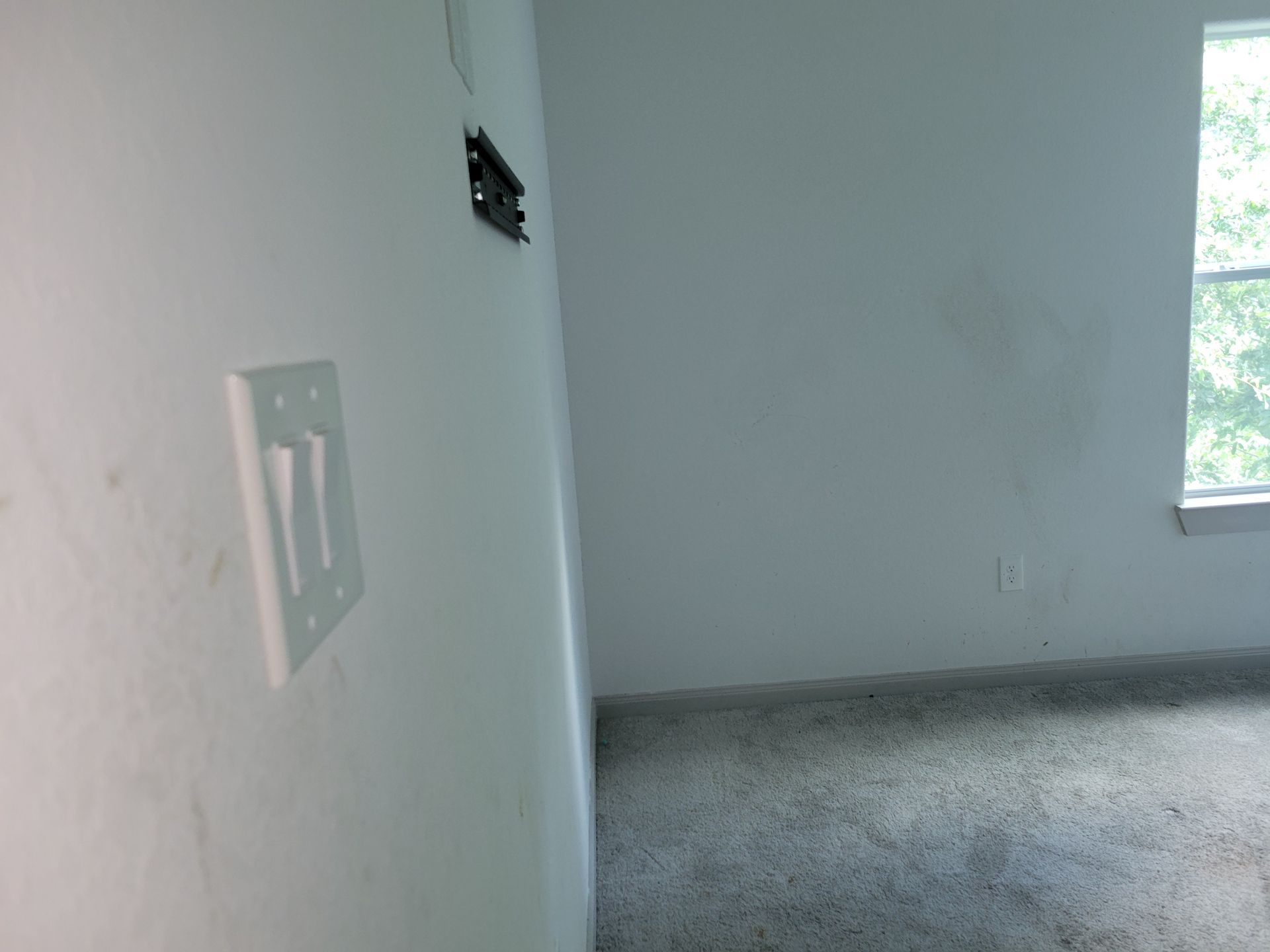 Interior view: white walls, light switch, exposed wiring, window, carpeted floor.