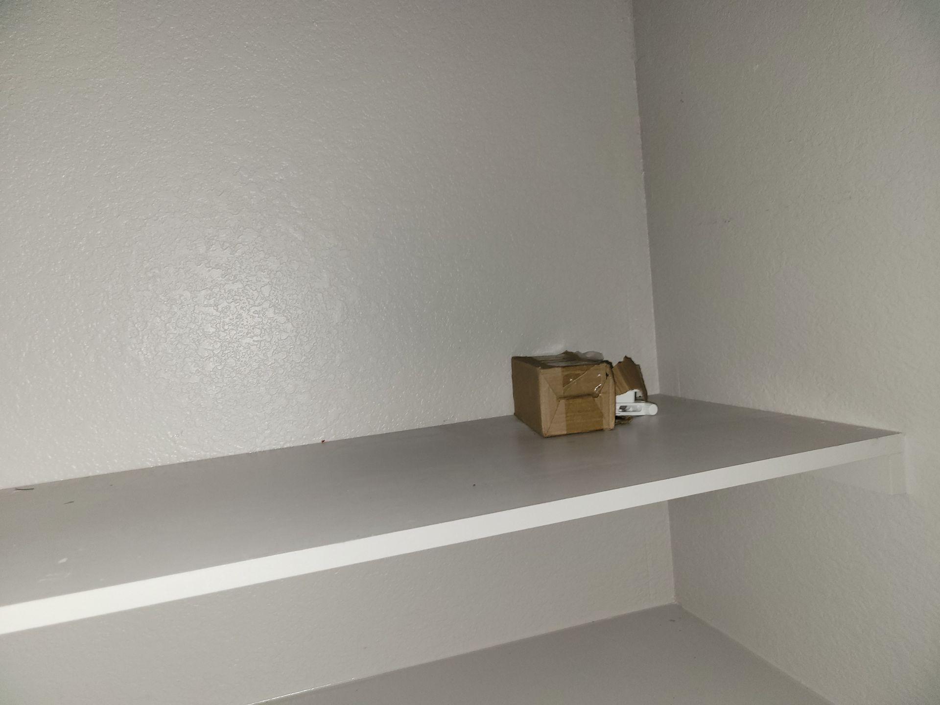 White shelf with a small cardboard box, inside a white closet.