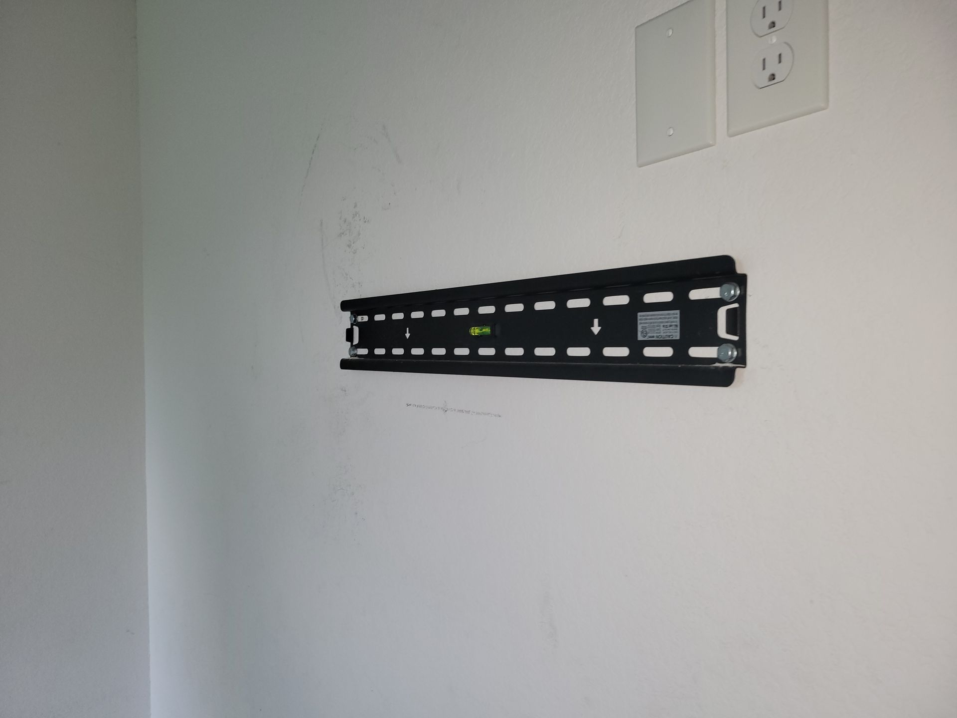 Black TV mount attached to a white wall, near electrical outlets.