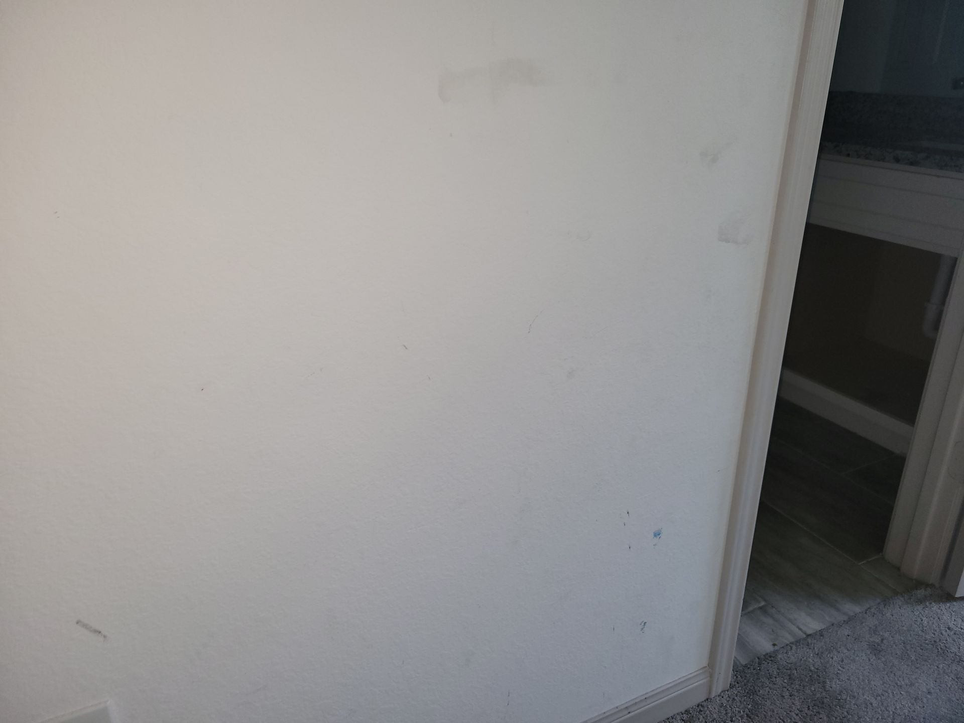 White wall with minor imperfections, a doorway on the right side, and carpeted floor visible.