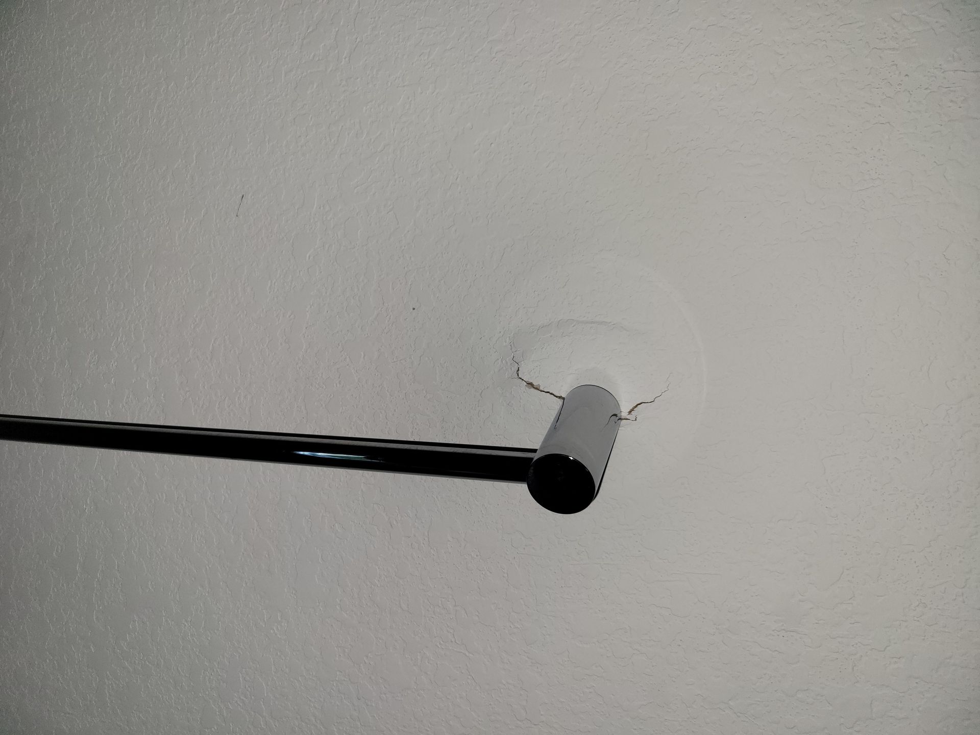 A black rod attached to a white ceiling, with a hole in the ceiling above the rod.