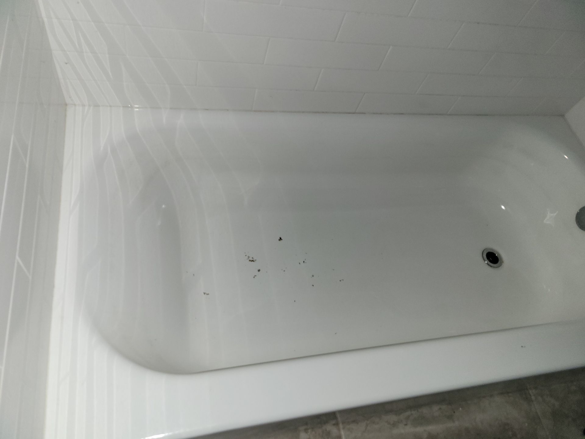 White bathtub with dark spots, viewed from above, in a bathroom with tiled walls and floor.