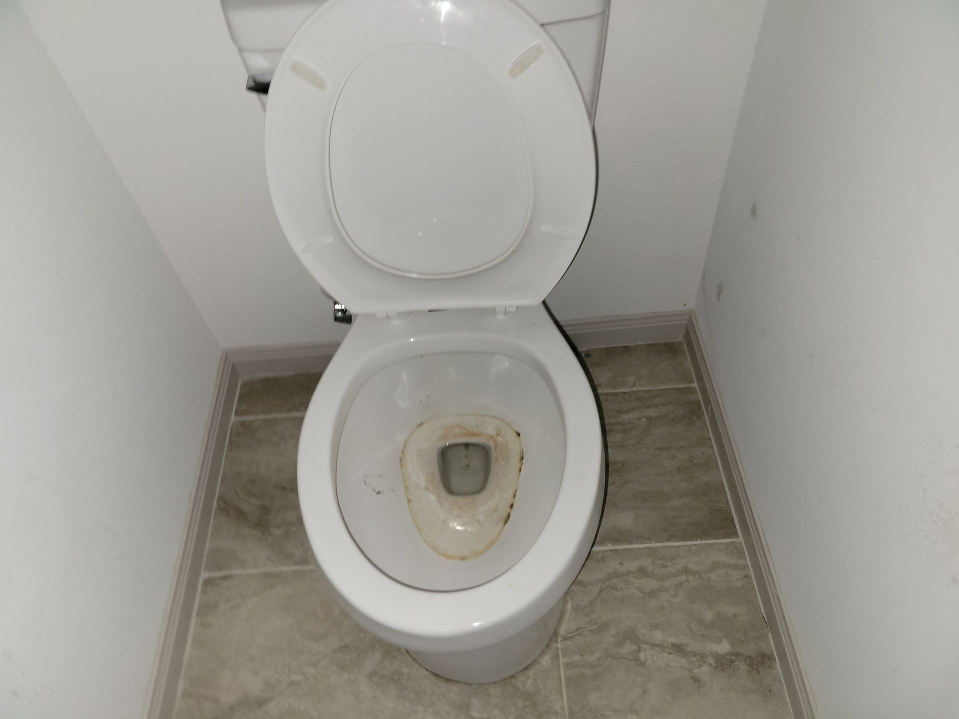 White toilet with the seat up in a small bathroom with tile flooring and white walls.