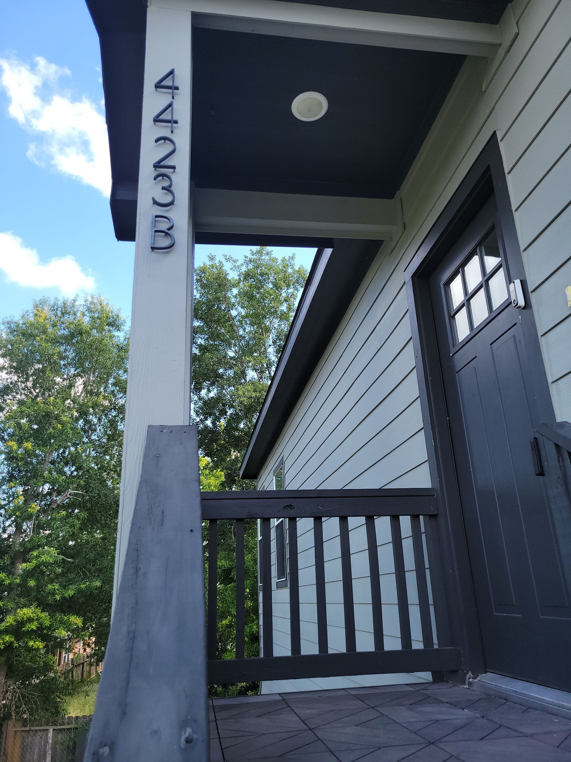 House entrance with address numbers 4233 on a column. Gray and green siding, dark door and railing.