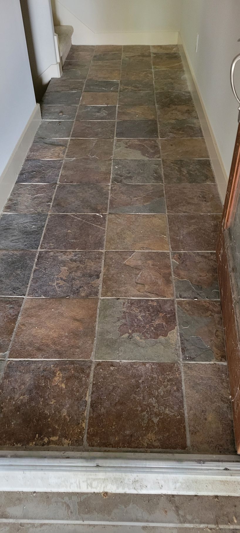A narrow hallway with brown square tiles on the floor. White walls.