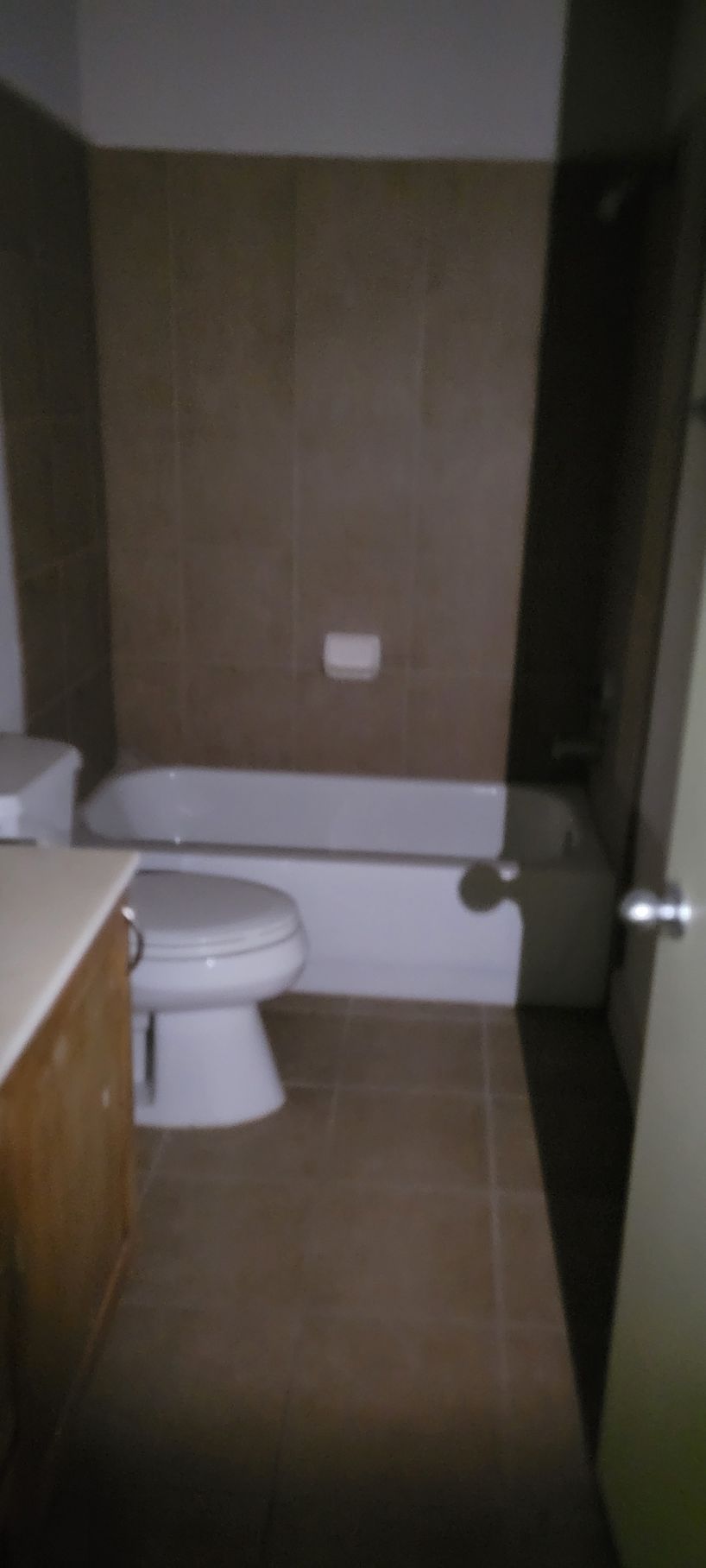Bathroom with a white bathtub and toilet, brown tile floor and wall.