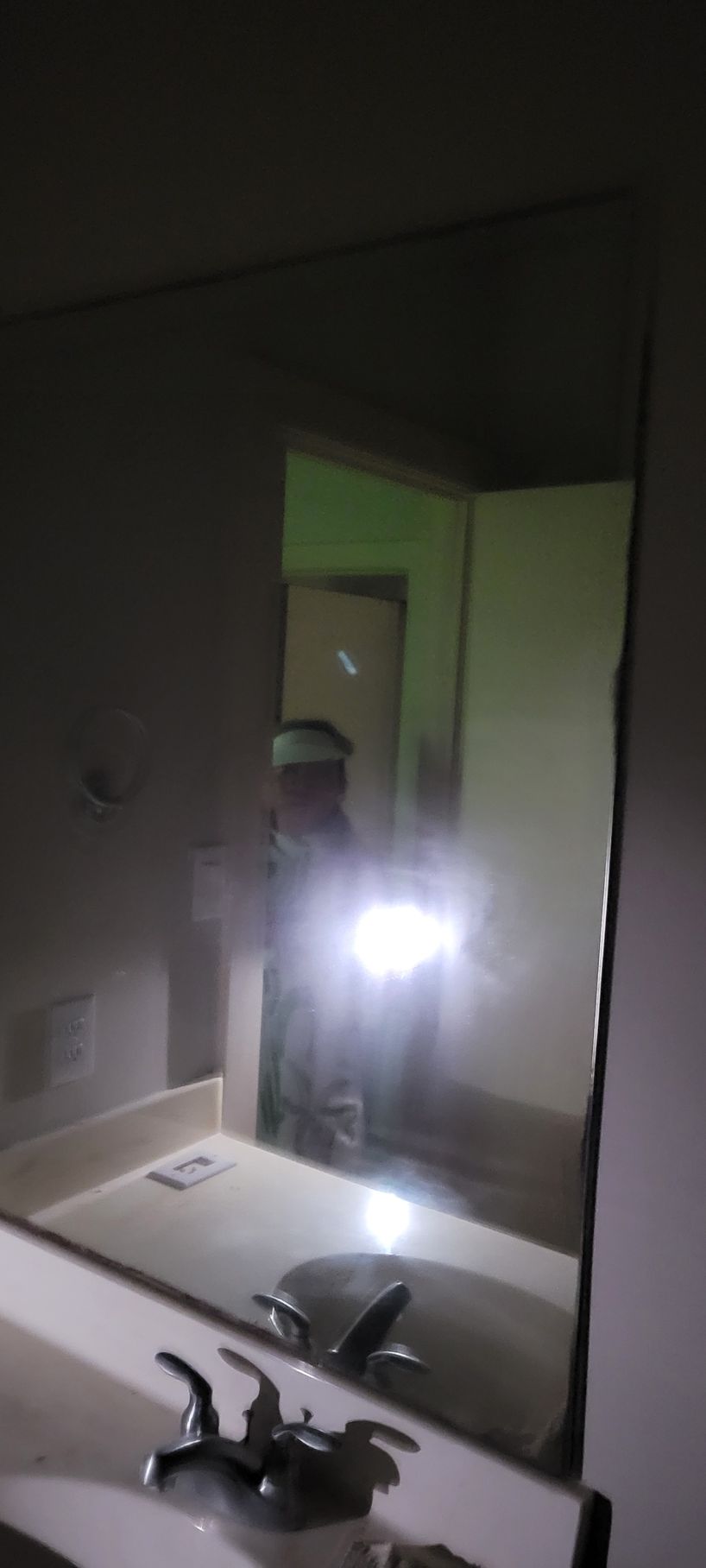 Mirror reflecting a person holding a bright light in a bathroom. Faucet is visible in the foreground.