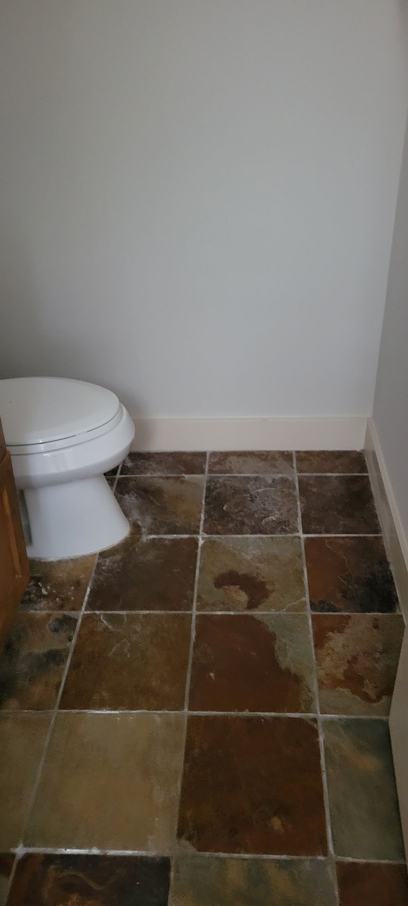 A bathroom with a toilet and square, multi-colored tiles on the floor. White walls.
