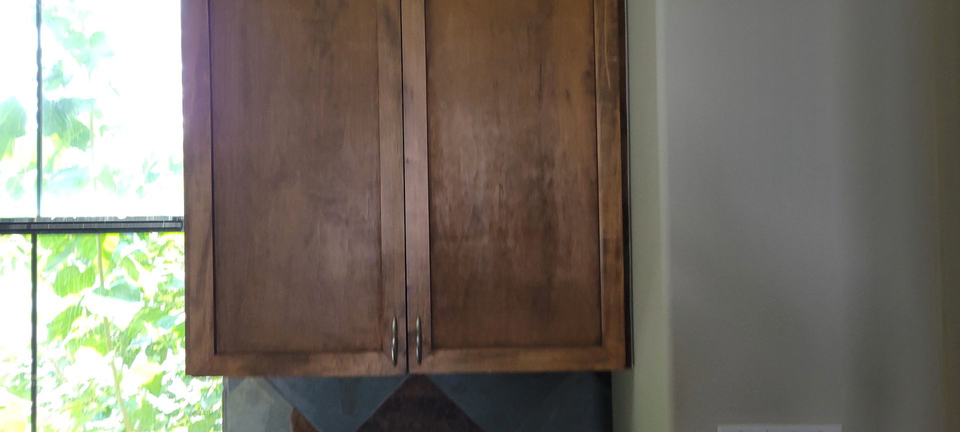 Wooden kitchen cabinets above a window with a view of green foliage.