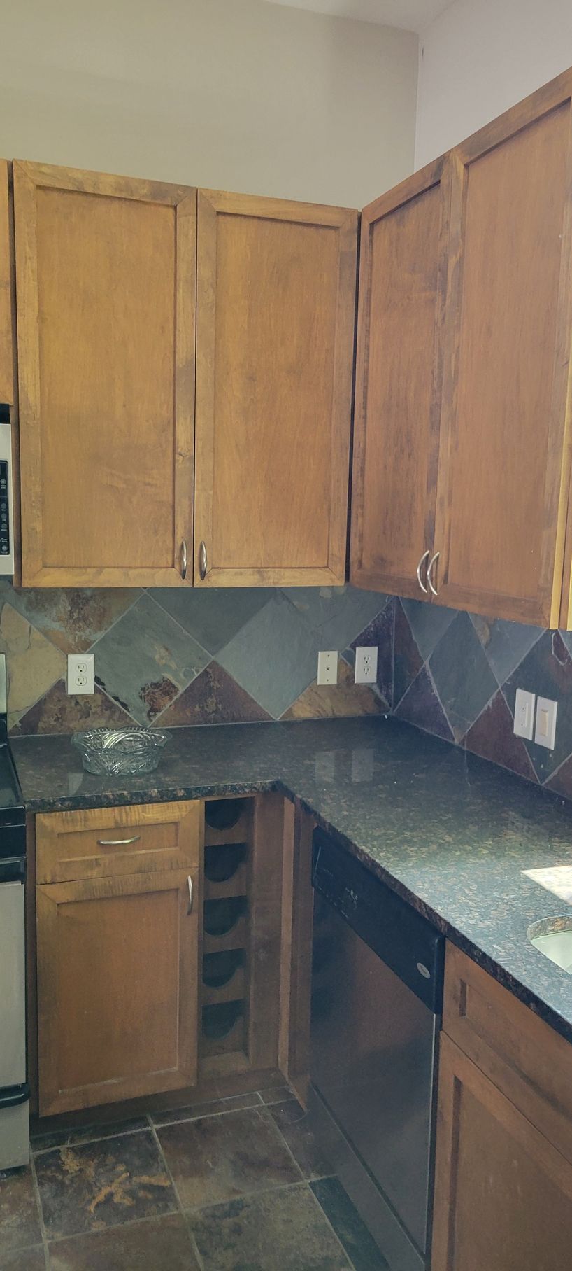 A kitchen with wooden cabinets, a dark countertop, and tiled backsplash. A dishwasher is present.
