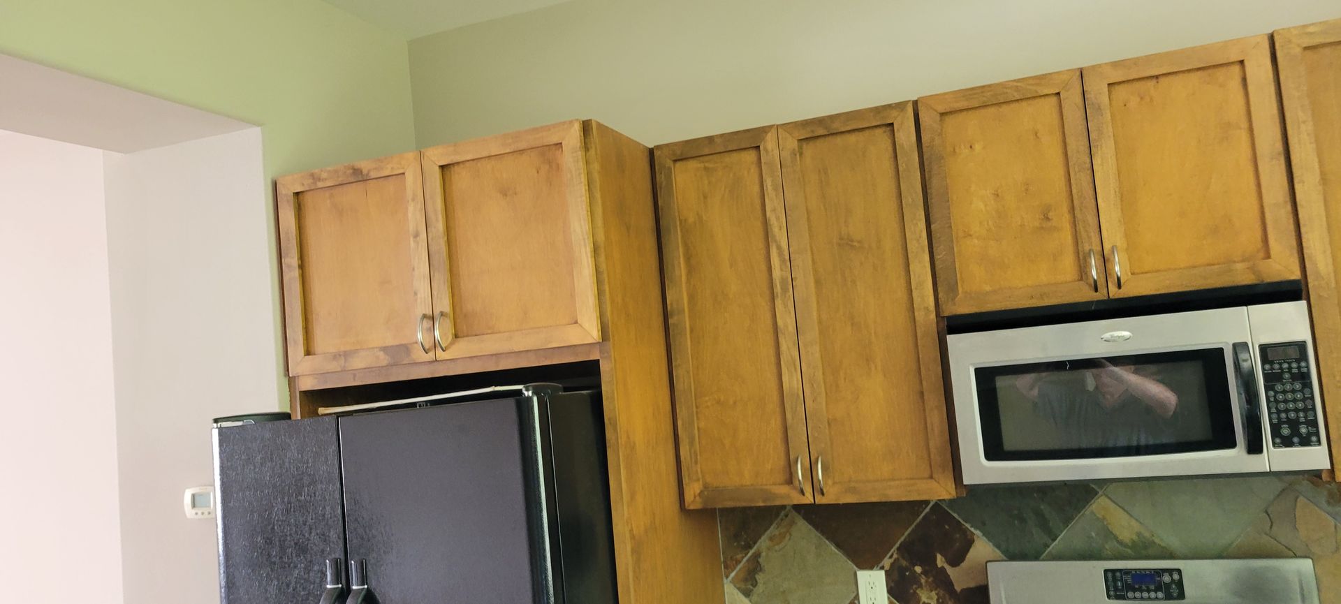 Kitchen with wooden cabinets, a microwave, and a black refrigerator. The walls are light green and cream.
