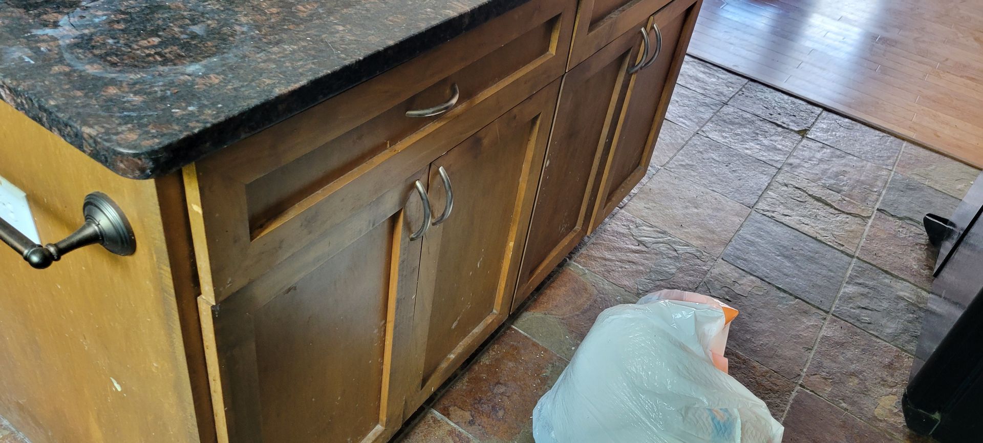 Cabinet with dark countertop, ornate metal towel bar. Brown cabinets, tile floor.