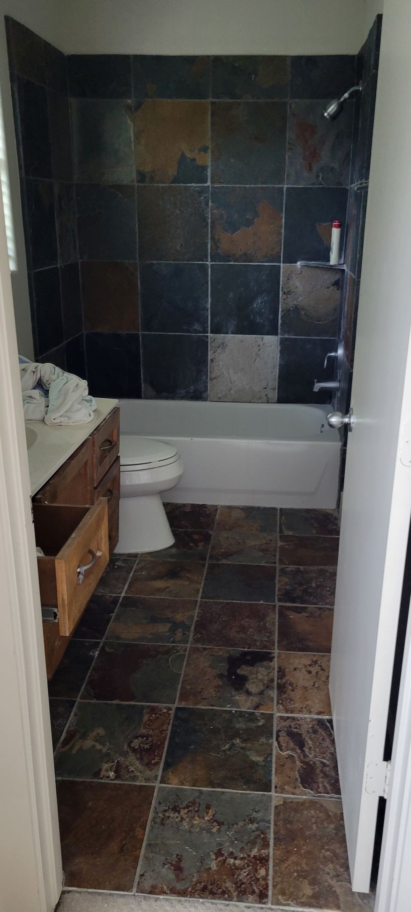 Bathroom with slate tile shower and flooring. Brown vanity, white toilet and bathtub.