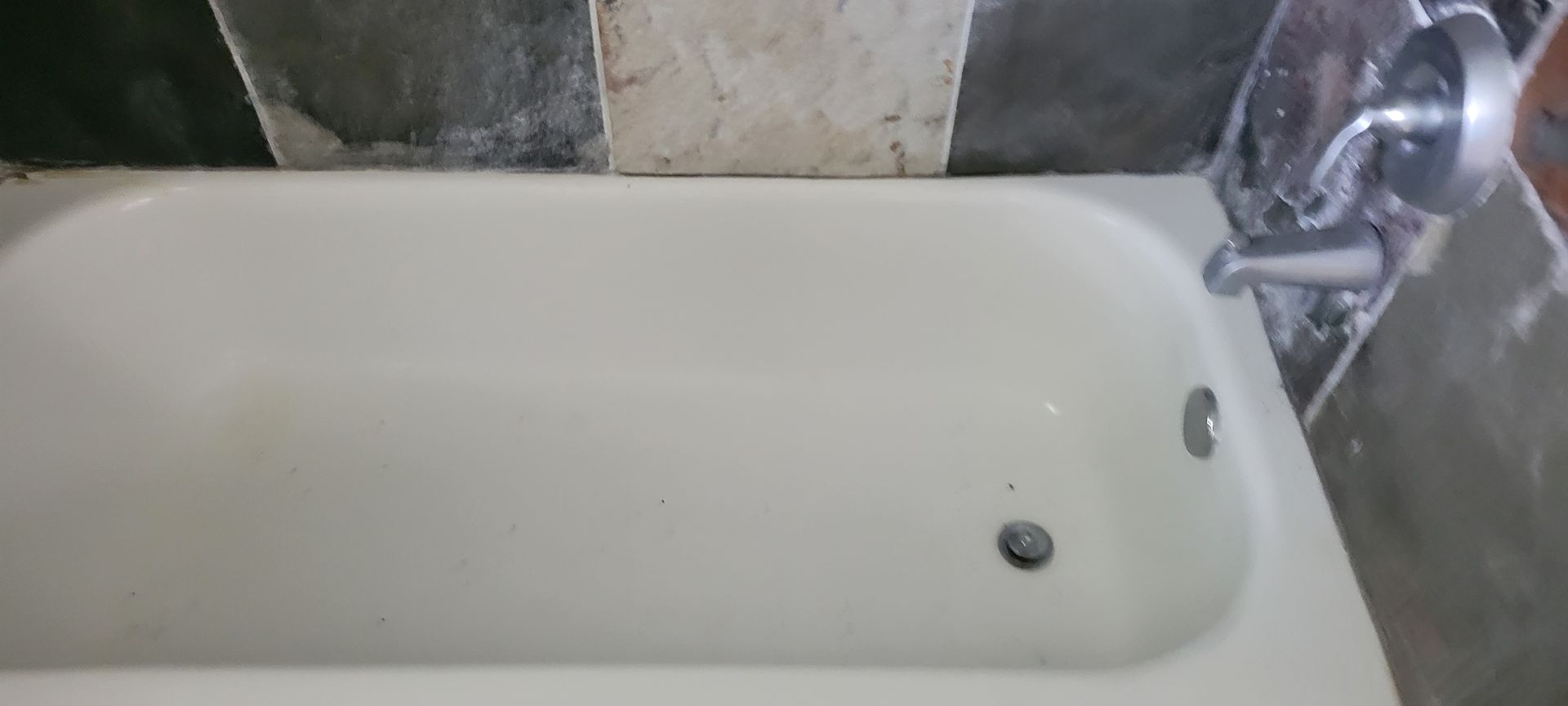 White bathtub with chrome fixtures; unfinished wall behind the tub.