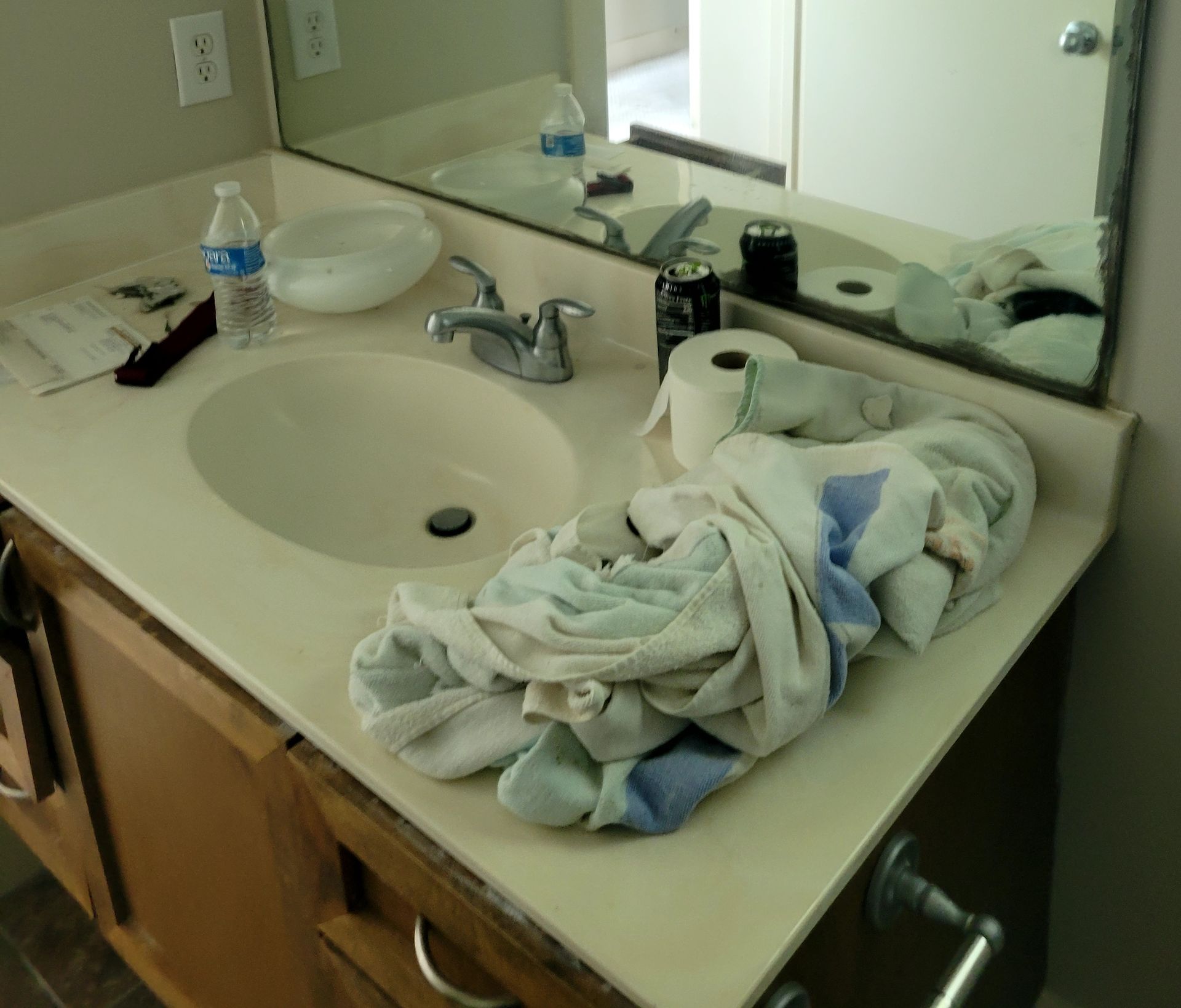 Bathroom sink with towels, toiletries, and water bottle on the countertop. Mirror reflects some items.